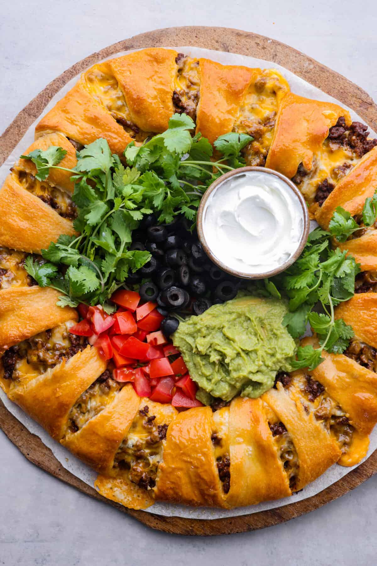 This taco ring is the easiest, cheesiest dinner. I know your family will love it as much as mine does! All you need is a can of crescent rolls, shredded Colby Jack cheese, some taco seasoning, and your favorite fixings to bring it to life! A whole taco ring, filled with servings of guacamole, sour cream, cilantro, tomatoes, and olives.