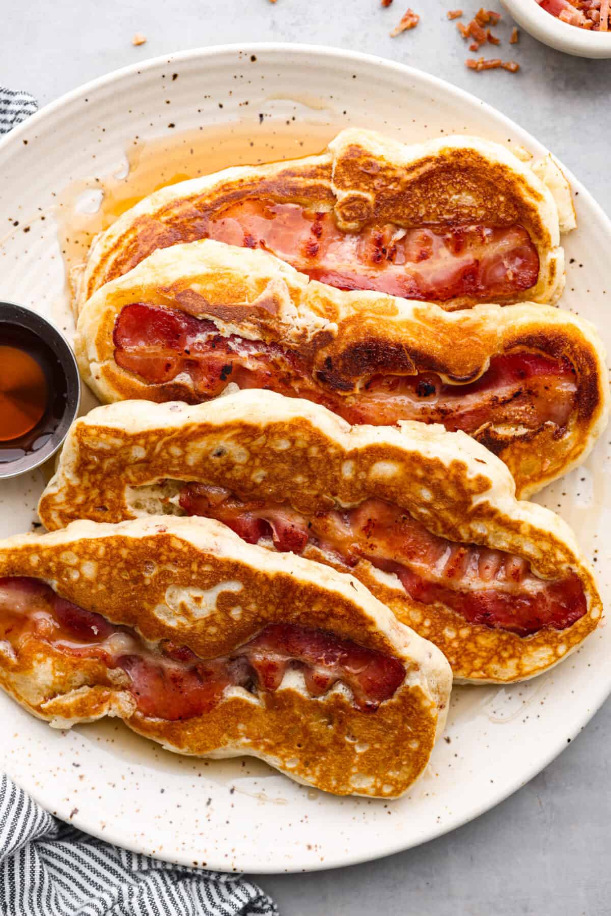 An all-in-one breakfast, and so good, you won't be able to get enough. Crispy bacon nestled in pillowy pancakes, topped with butter and syrup - what could be better? 4 bacon pancakes on a plate.