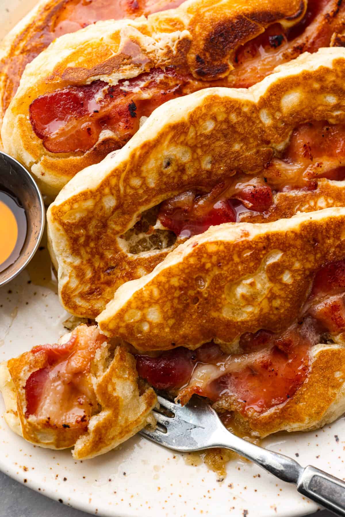 An all-in-one breakfast, and so good, you won't be able to get enough. Crispy bacon nestled in pillowy pancakes, topped with butter and syrup - what could be better? Closeup of a bite of a bacon pancake.