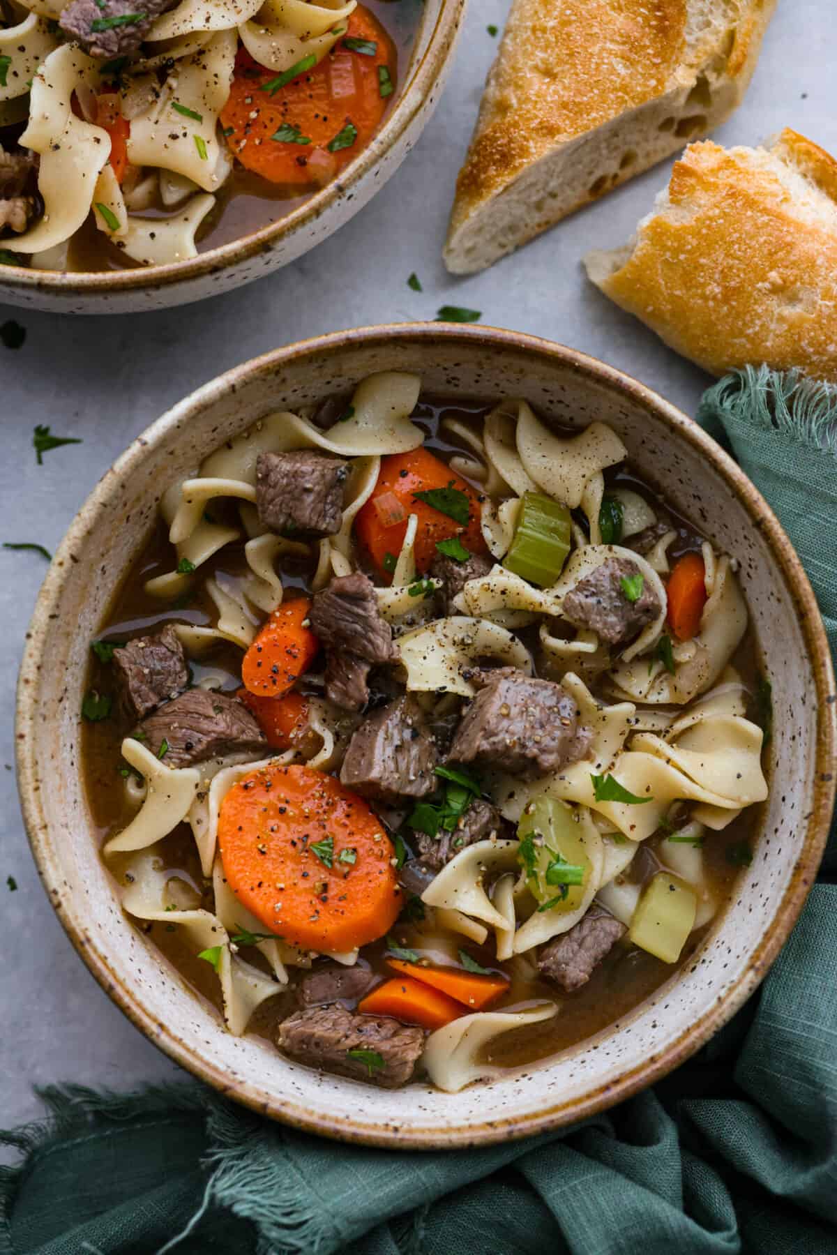 Warm and comforting Beef Noodle Soup is a delicious spin off of classic chicken noodle soup. A combination of tender beef, vegetables and egg noodles is simmered in a savory broth for the best one-pot winter meal! Top-down view of beef noodle soup in a stoneware bowl.