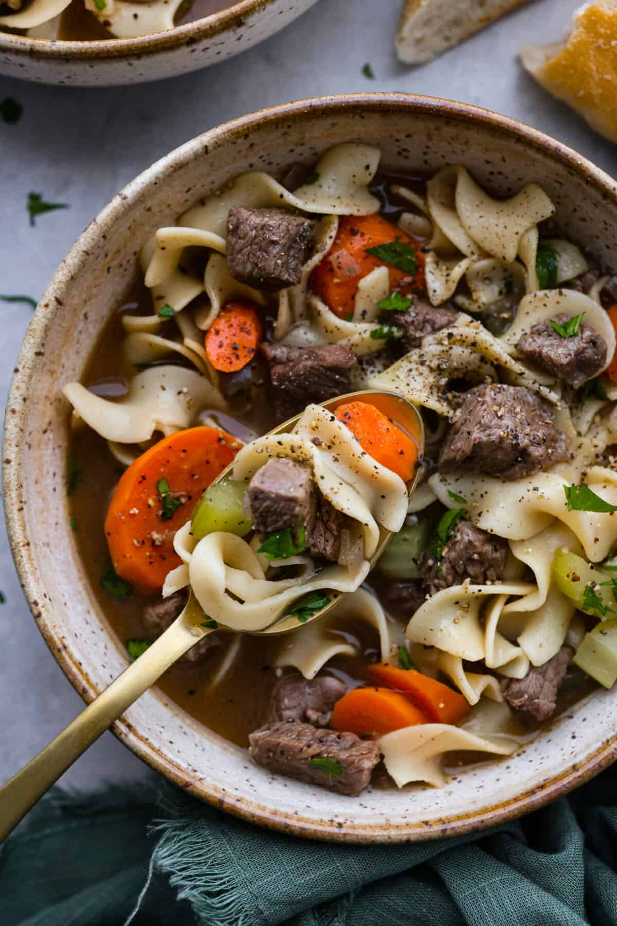 Warm and comforting Beef Noodle Soup is a delicious spin off of classic chicken noodle soup. A combination of tender beef, vegetables and egg noodles is simmered in a savory broth for the best one-pot winter meal! Closeup of soup in a gold metal spoon.
