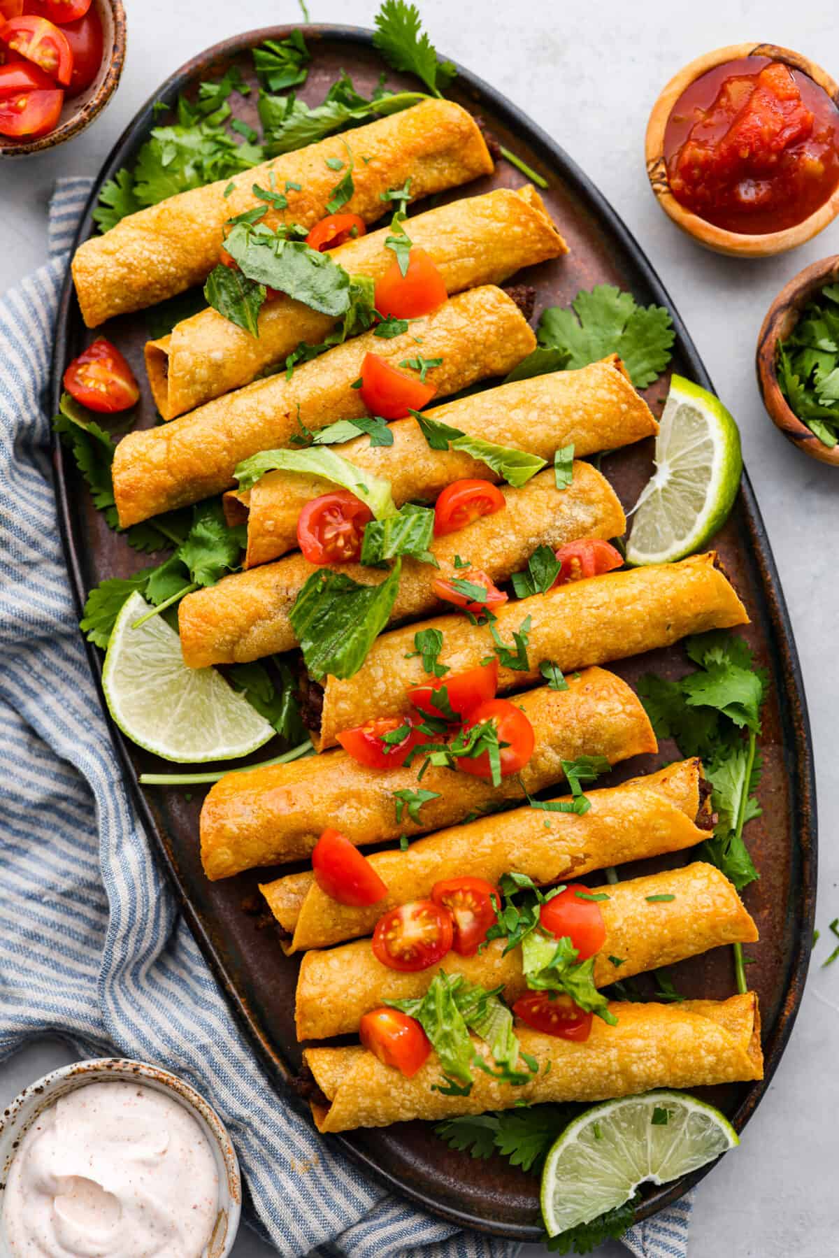 Cook up a batch of these homemade beef taquitos, you won't be disappointed! The meaty, cheesy filling and crispy tortilla shell are to die for. A million times better than the frozen kind! Beef taquitos on a black serving dish.