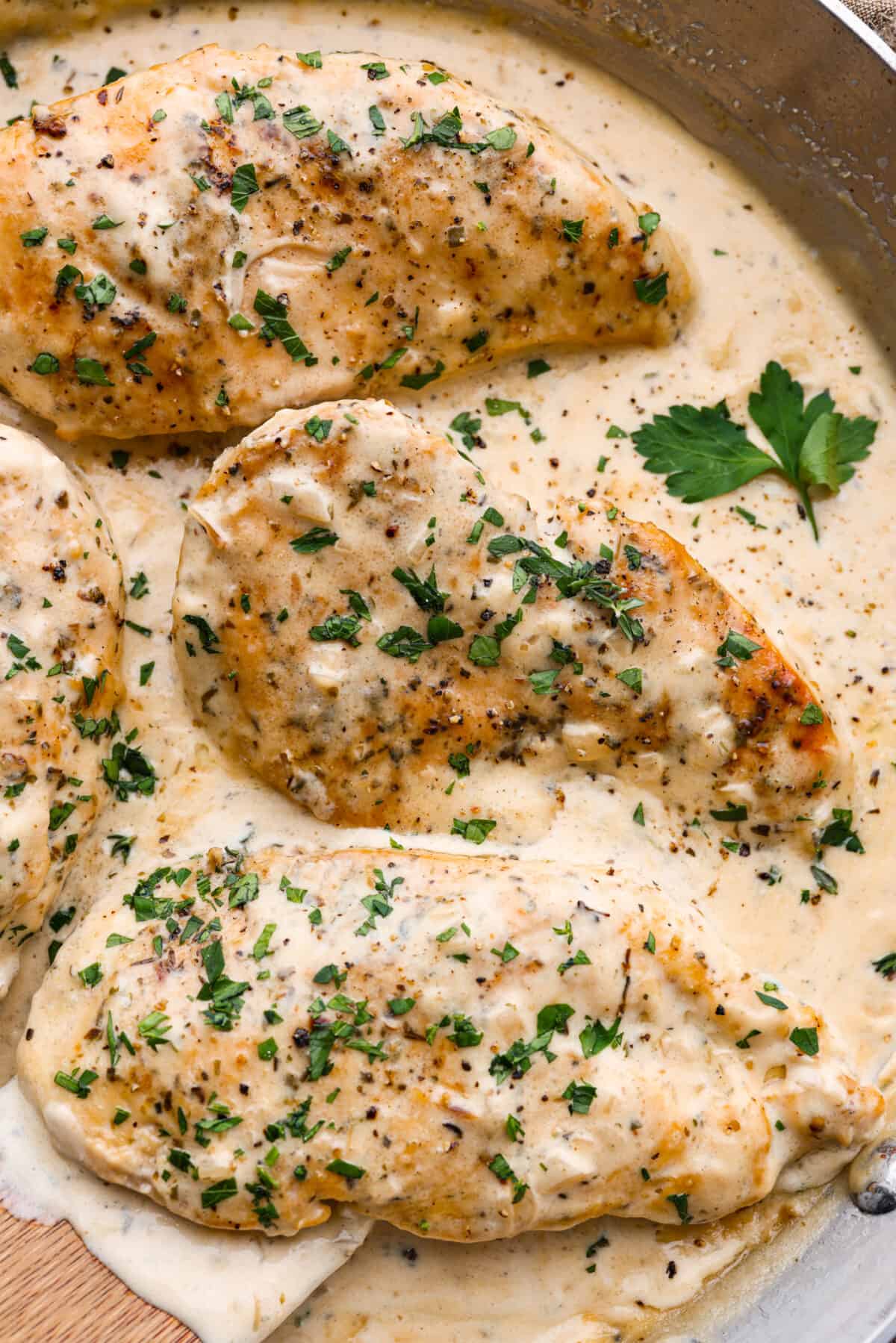 Creamy Boursin Chicken is a rich and decadent one-pan dish that is ready in just about 30 minutes! Pan-fried, seasoned chicken is smothered in a delicious sauce made with cream, parmesan cheese and Boursin cheese. Closeup of 3 cooked chicken breasts, covered in a creamy sauce and topped with fresh herbs.
