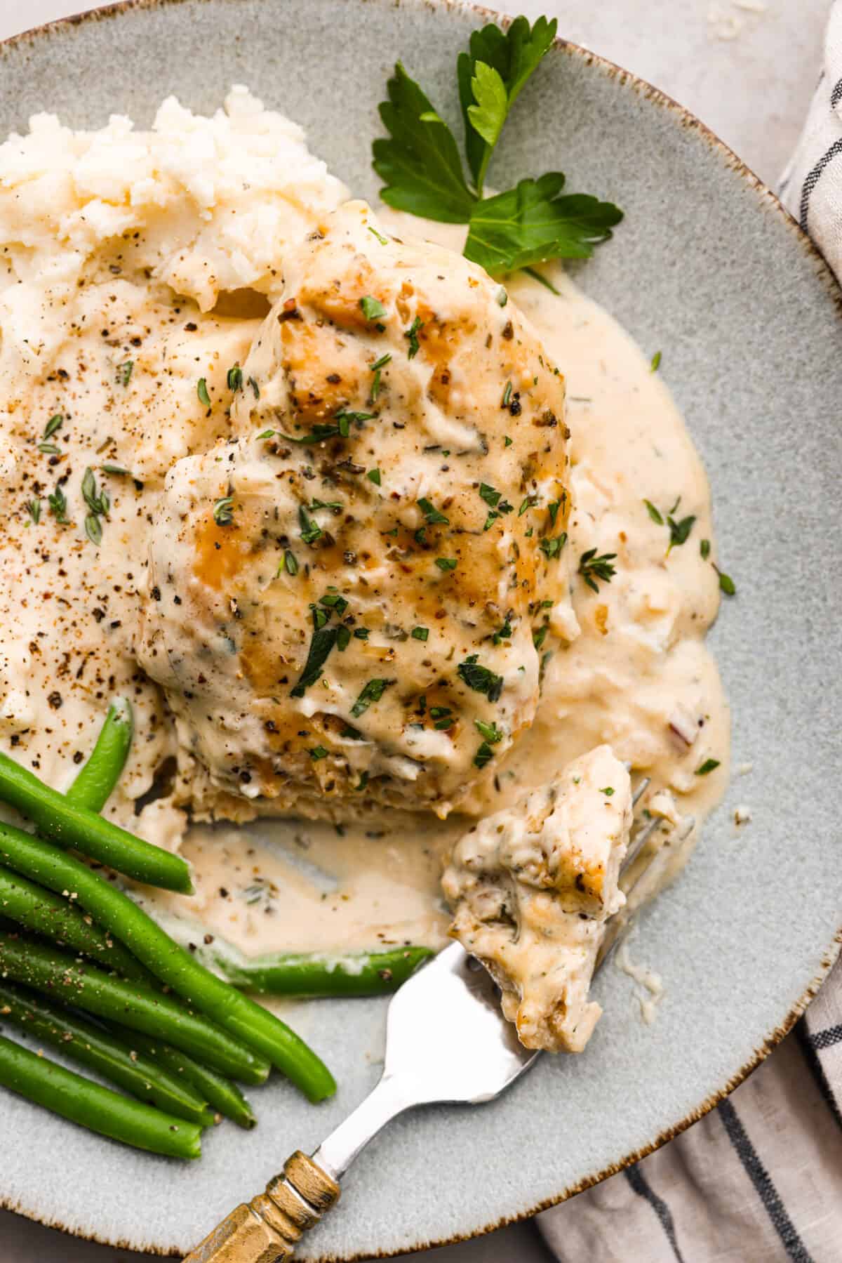 Creamy Boursin Chicken is a rich and decadent one-pan dish that is ready in just about 30 minutes! Pan-fried, seasoned chicken is smothered in a delicious sauce made with cream, parmesan cheese and Boursin cheese. Boursin chicken served on a gray plate with green beans and mashed potatoes.
