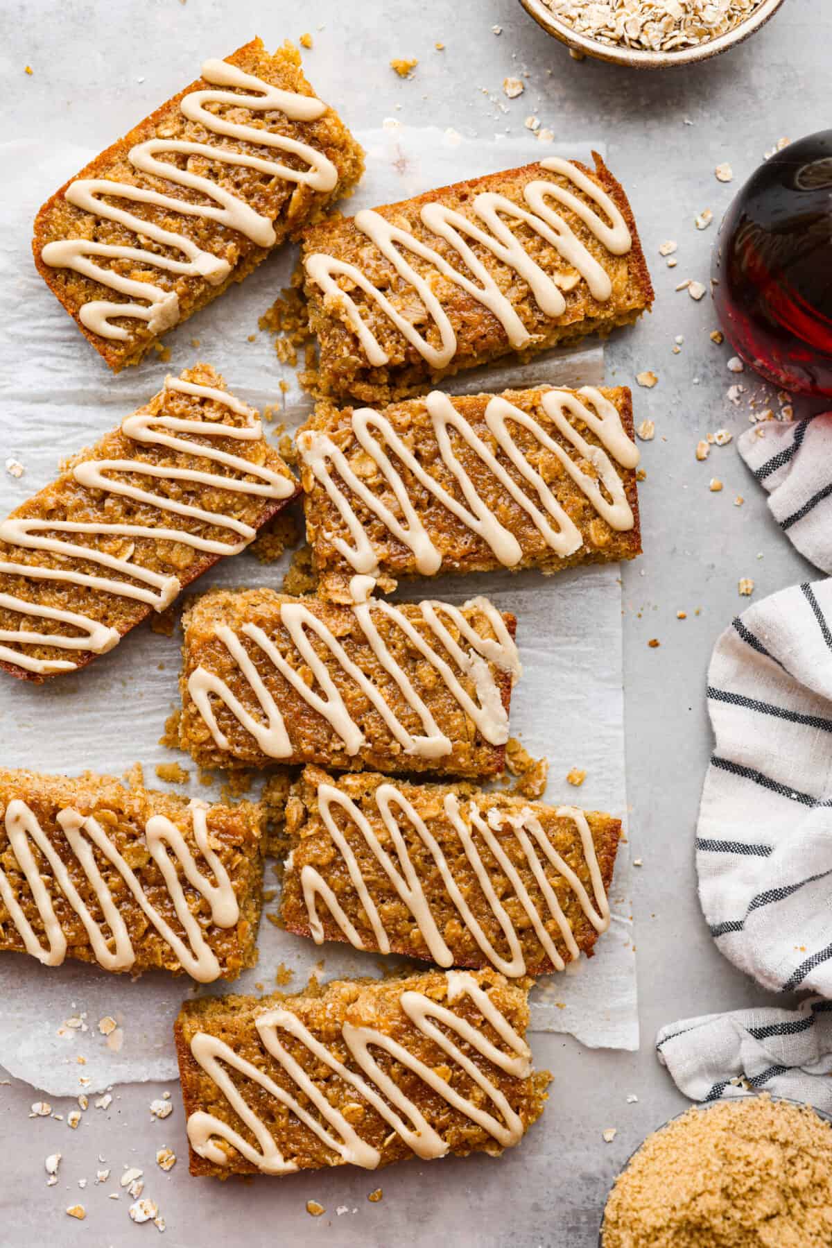 Start your day right with these simple and delicious Oatmeal Breakfast Bars. Topped with a sweet brown sugar maple glaze, these bars are easy to whip up and guaranteed to be a hit for a wholesome morning treat. Breakfast bars on some parchment paper on the countertop.