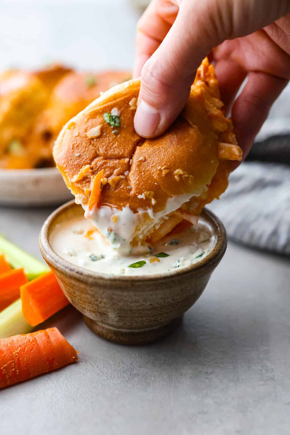 Whether it's a weeknight dinner or a casual get-together, everyone will love the spicy rotisserie chicken sandwiched between soft dinner rolls with ranch dressing, melted cheese, and crunchy coleslaw. A buffalo chicken slider being dipped into ranch sauce.