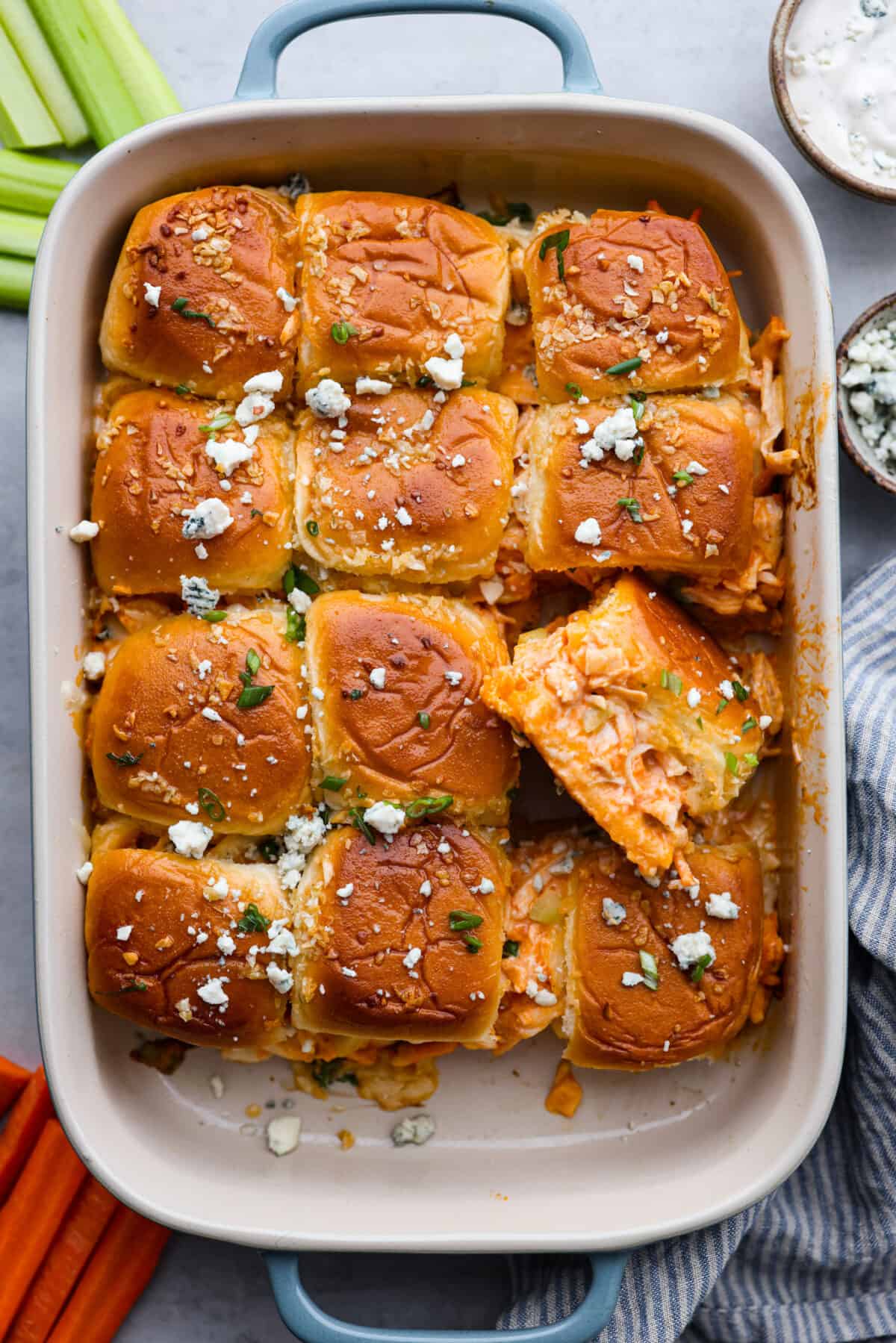 Whether it's a weeknight dinner or a casual get-together, everyone will love the spicy rotisserie chicken sandwiched between soft dinner rolls with ranch dressing, melted cheese, and crunchy coleslaw. The top view of sliders in a casserole dish. one is pulled out and turned so that you can see the inside of the roll.