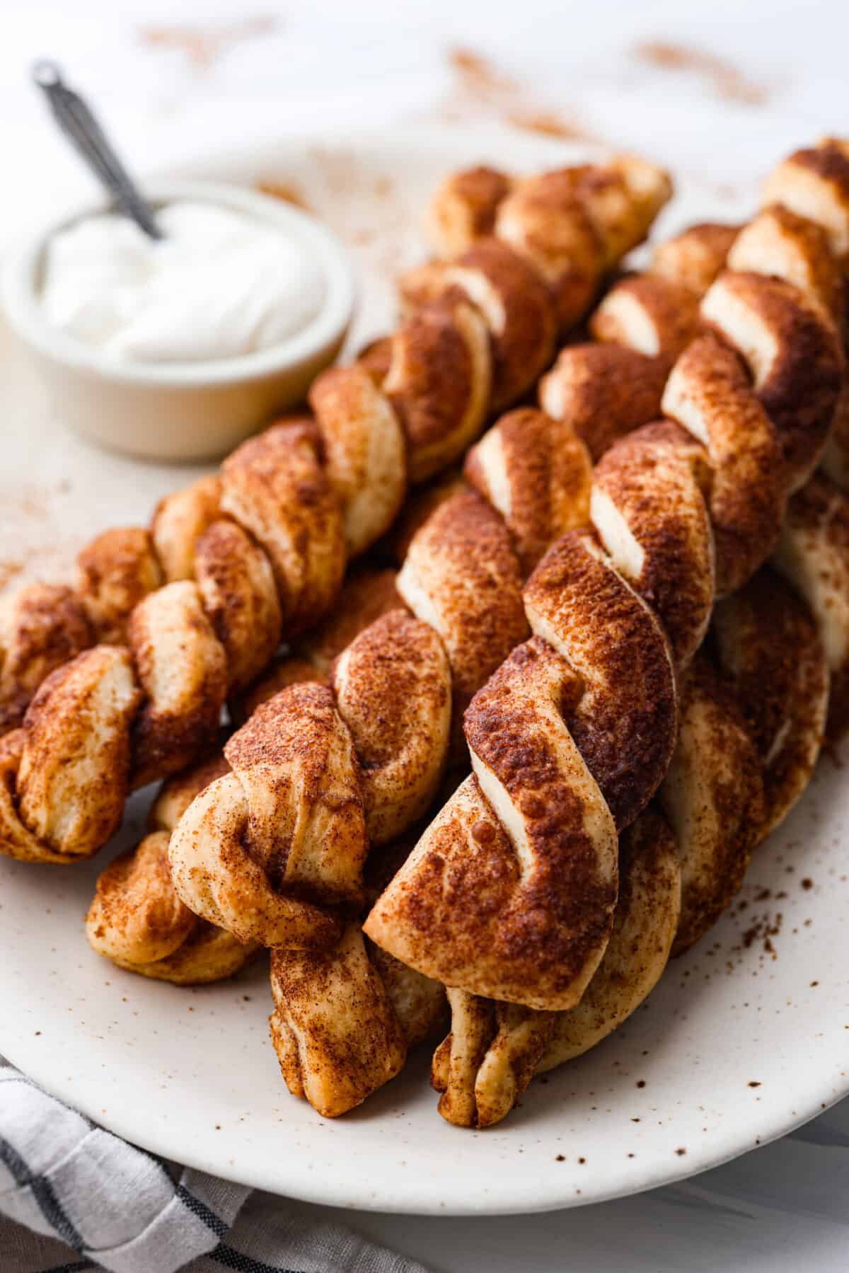 Everyone LOVES these sweet and fluffy cinnamon roll breadtwists. Homemade dough twisted and baked in brown sugar cinnamon goodness. It's like eating the middle of a cinnamon roll! Perfect for breakfast, enjoy as a snack, or delicious as a dessert. Close view of cinnamon roll breadtwists stacked on a plate.