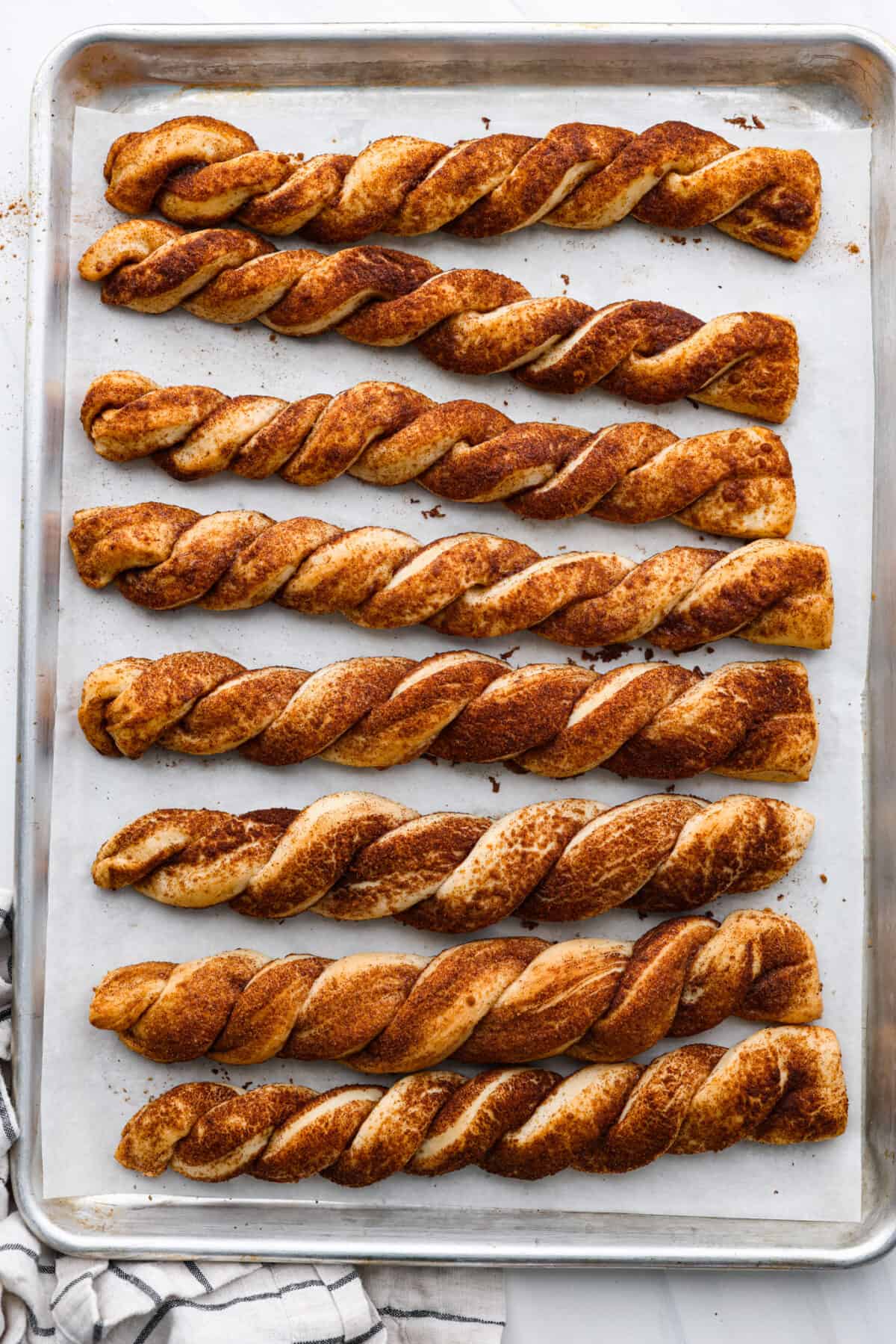 Everyone LOVES these sweet and fluffy cinnamon roll breadtwists. Homemade dough twisted and baked in brown sugar cinnamon goodness. It's like eating the middle of a cinnamon roll! Perfect for breakfast, enjoy as a snack, or delicious as a dessert. Top view of the bread twists baked on a baking sheet.