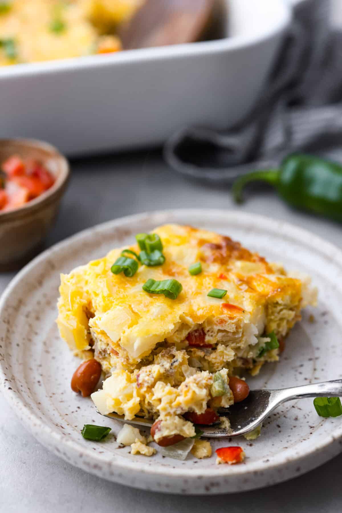Cowboy breakfast casserole is a hearty dish that's chock full of breakfast favorites (eggs, bacon, sausage, beans, cheese, potatoes, and more!) and super easy to make! A slice of the breakfast bake with a bite taken out of it