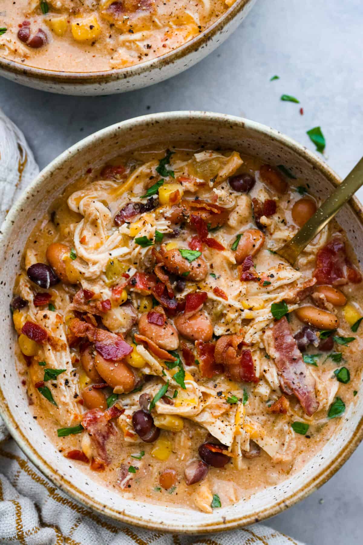 Creamy crack chicken chili is an explosion of irresistible flavors! It's loaded with shredded chicken, tender beans, corn, AND all your favorite crack-inspired ingredients. This is our new favorite chili recipe and we can't get enough of it! Close top view of chili in a bowl with a spoon.