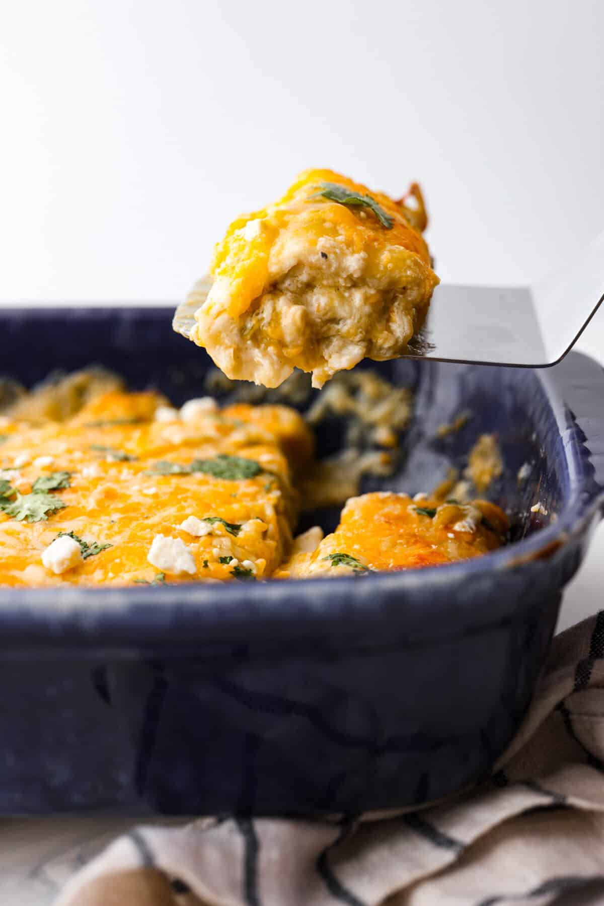 Creamy and flavorful, these cream cheese enchiladas are easy to make and always a crowd favorite! They are packed with chicken, three types of cheese, plenty of seasoning and green enchilada sauce for a meal that everyone will enjoy! Serving a cream cheese enchilada with a metal spatula.