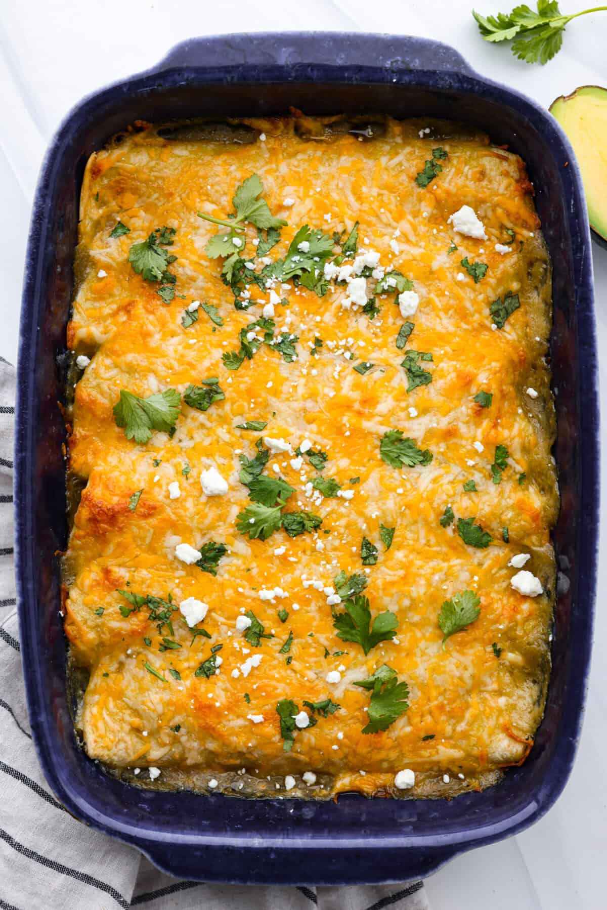 Creamy and flavorful, these cream cheese enchiladas are easy to make and always a crowd favorite! They are packed with chicken, three types of cheese, plenty of seasoning and green enchilada sauce for a meal that everyone will enjoy! Top-down view of cream cheese enchiladas in a blue baking dish.