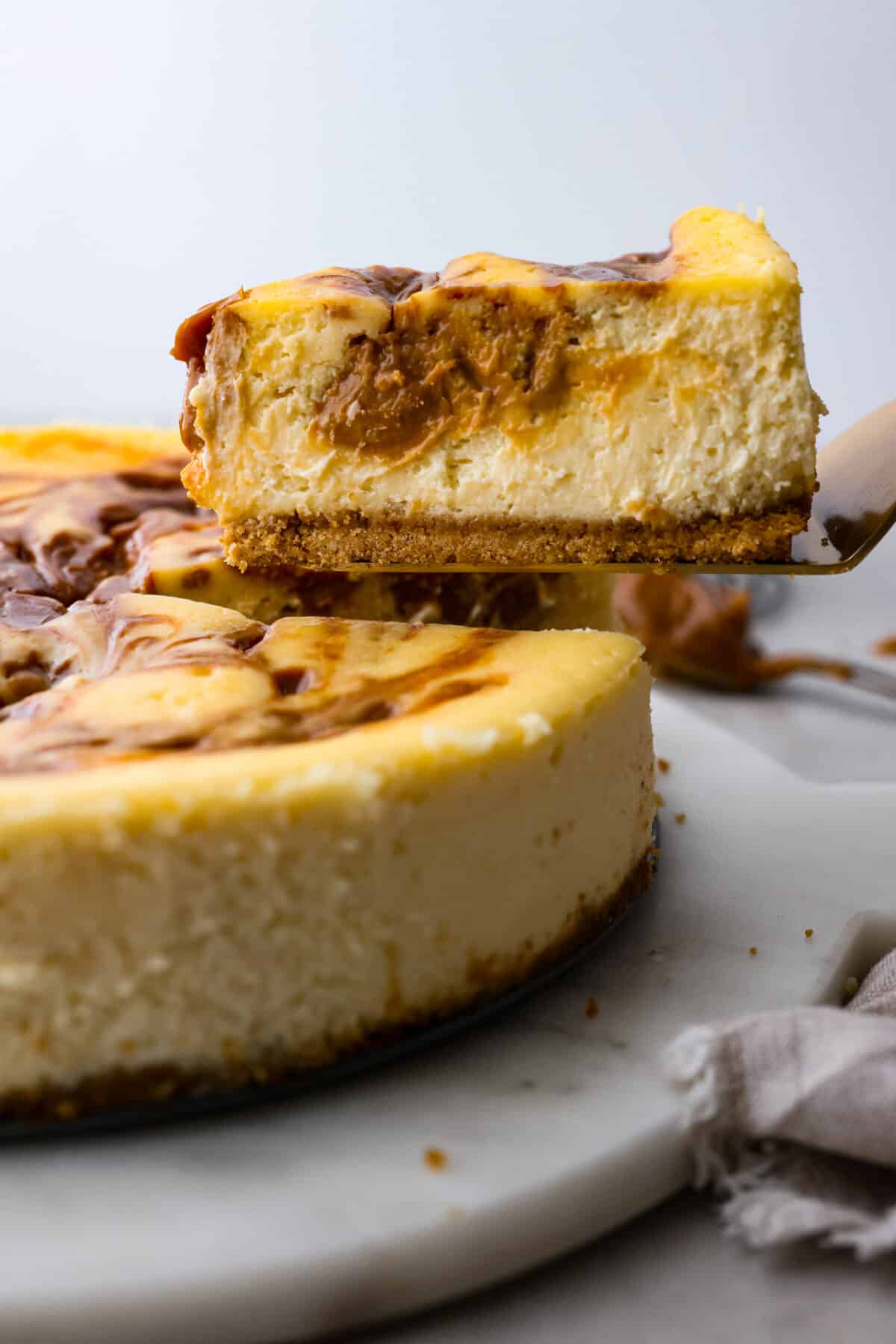 Dulce de leche cheesecake is the most creamy and decadent dessert, with swirls of caramel in every bite. It's guaranteed to be the star of your dinner table! A slice of cheesecake being served.