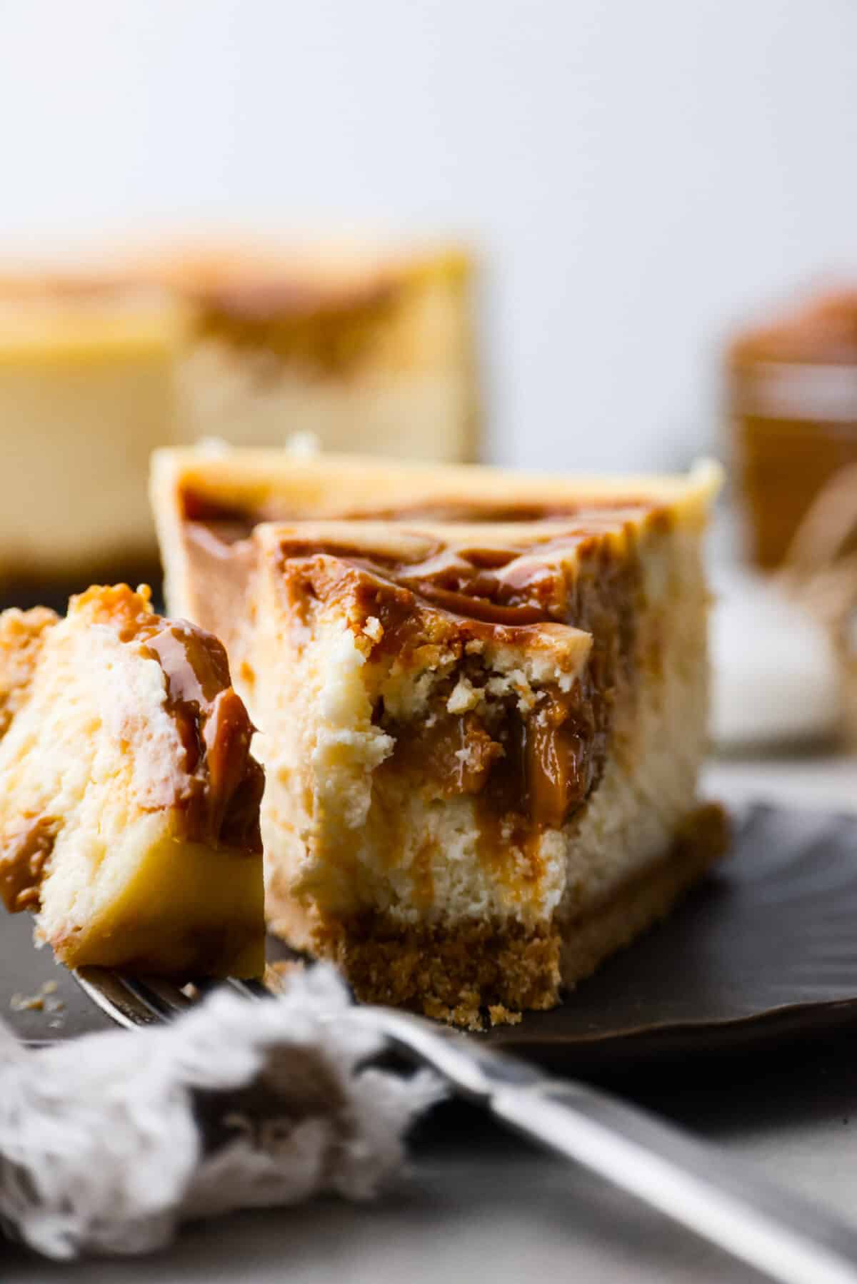 Dulce de leche cheesecake is the most creamy and decadent dessert, with swirls of caramel in every bite. It's guaranteed to be the star of your dinner table! Front view of a piece of cheesecake with a bite being taken out of it.