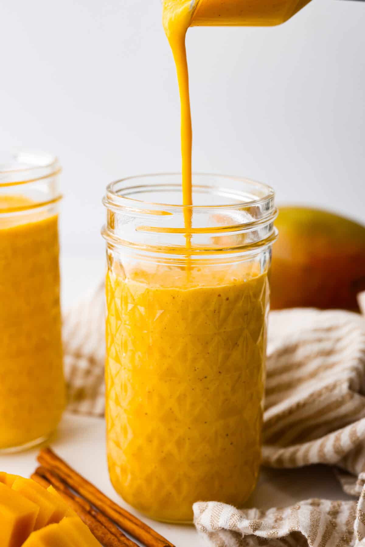 This creamy and sweet golden milk smoothie will brighten your morning! The smooth texture comes from the mangos, Greek yogurt, and banana. It's spiced to perfection and bursting with healthy benefits. Close view of golden milk smoothie pouring into a tall glass jar.