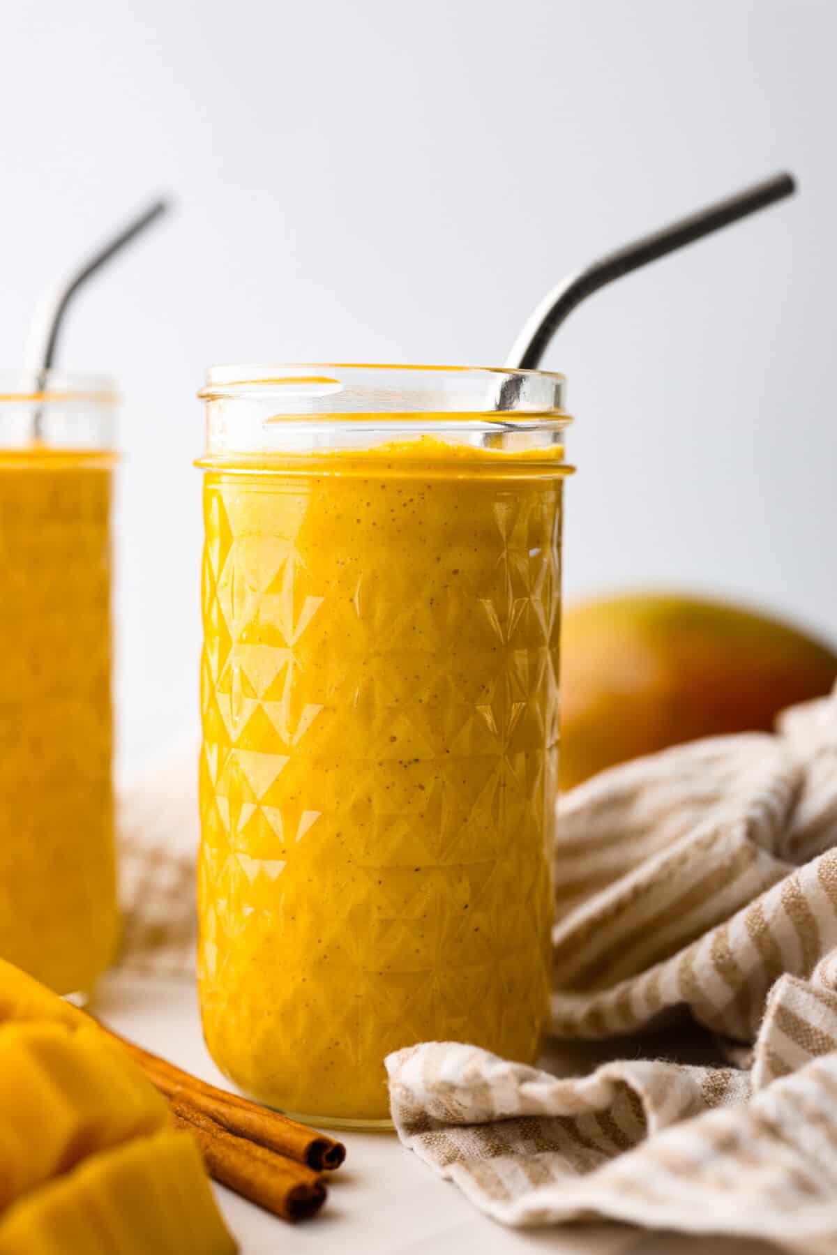 This creamy and sweet golden milk smoothie will brighten your morning! The smooth texture comes from the mangos, Greek yogurt, and banana. It's spiced to perfection and bursting with healthy benefits. Close side view of the golden milk smoothie in tall glass jars.