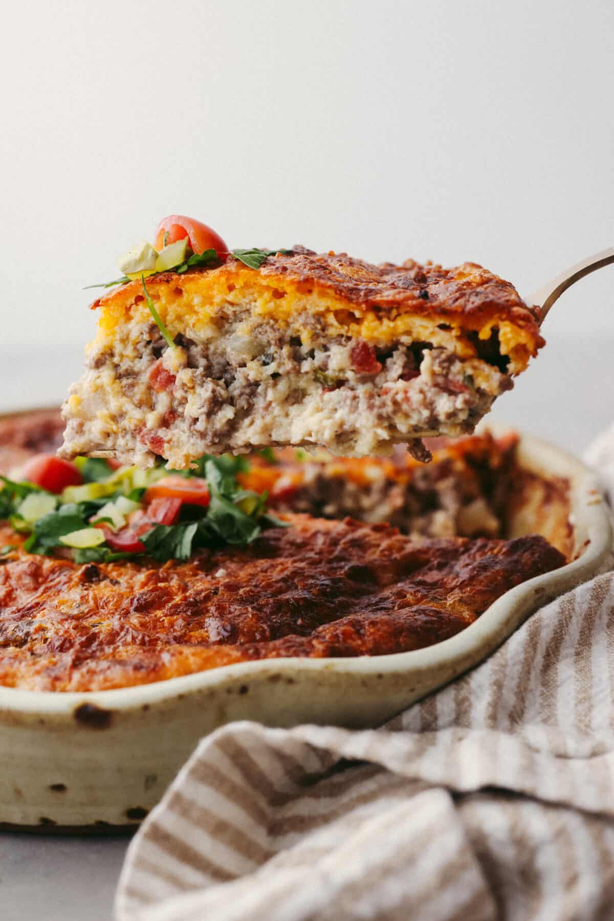 Impossible cheeseburger pie is an unexpected but TASTY twist on a cheeseburger! It's full of ground beef, and cheese, and the addition of Bisquick creates a comforting casserole texture. All your favorite hamburger ingredients are baked into a savory pie and your family will LOVE this version. Side view of a slice of cheeseburger pie lifting from the pie dish.