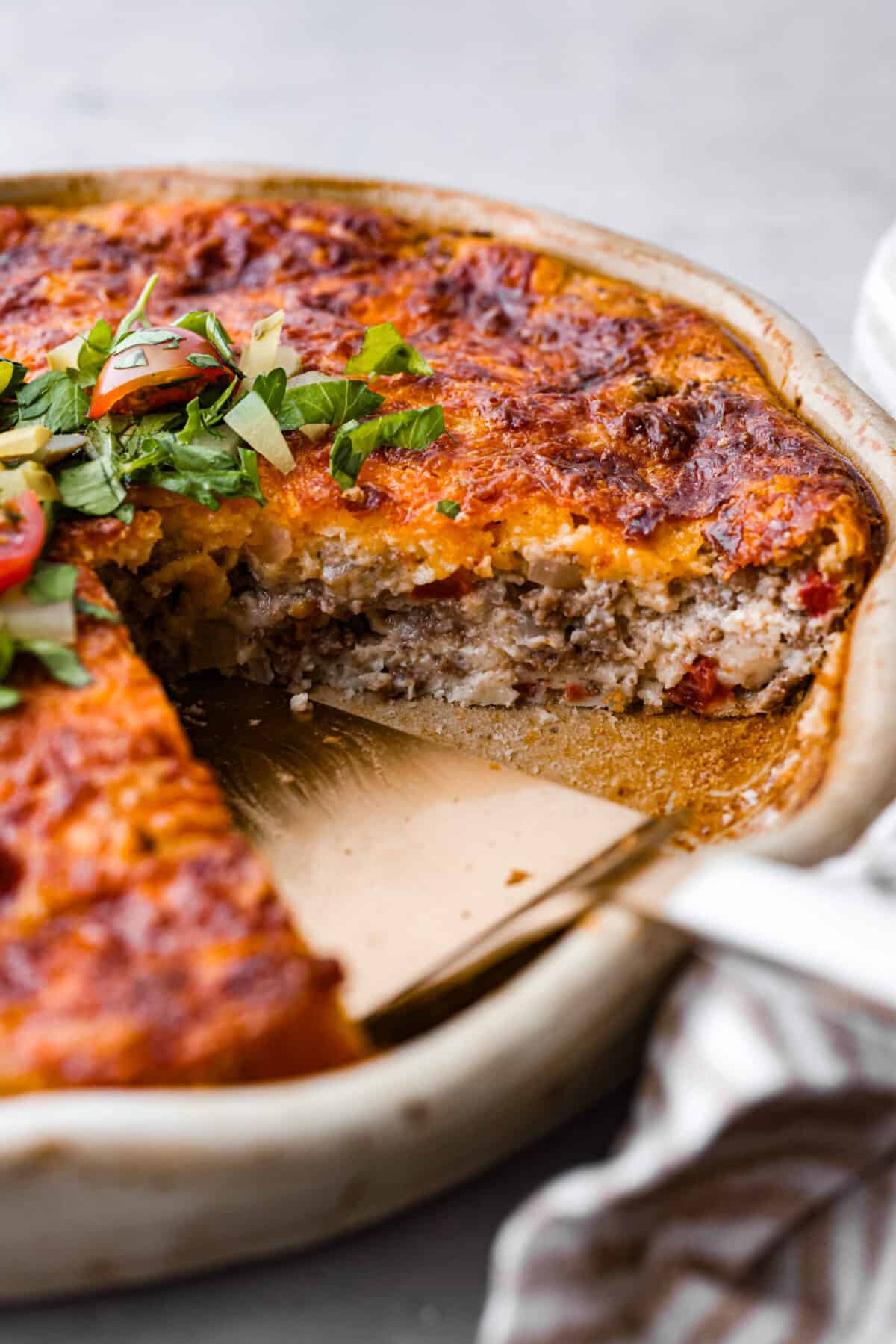 Impossible cheeseburger pie is an unexpected but TASTY twist on a cheeseburger! It's full of ground beef, and cheese, and the addition of Bisquick creates a comforting casserole texture. All your favorite hamburger ingredients are baked into a savory pie and your family will LOVE this version. Close view of cheeseburger pie in a pie dish.