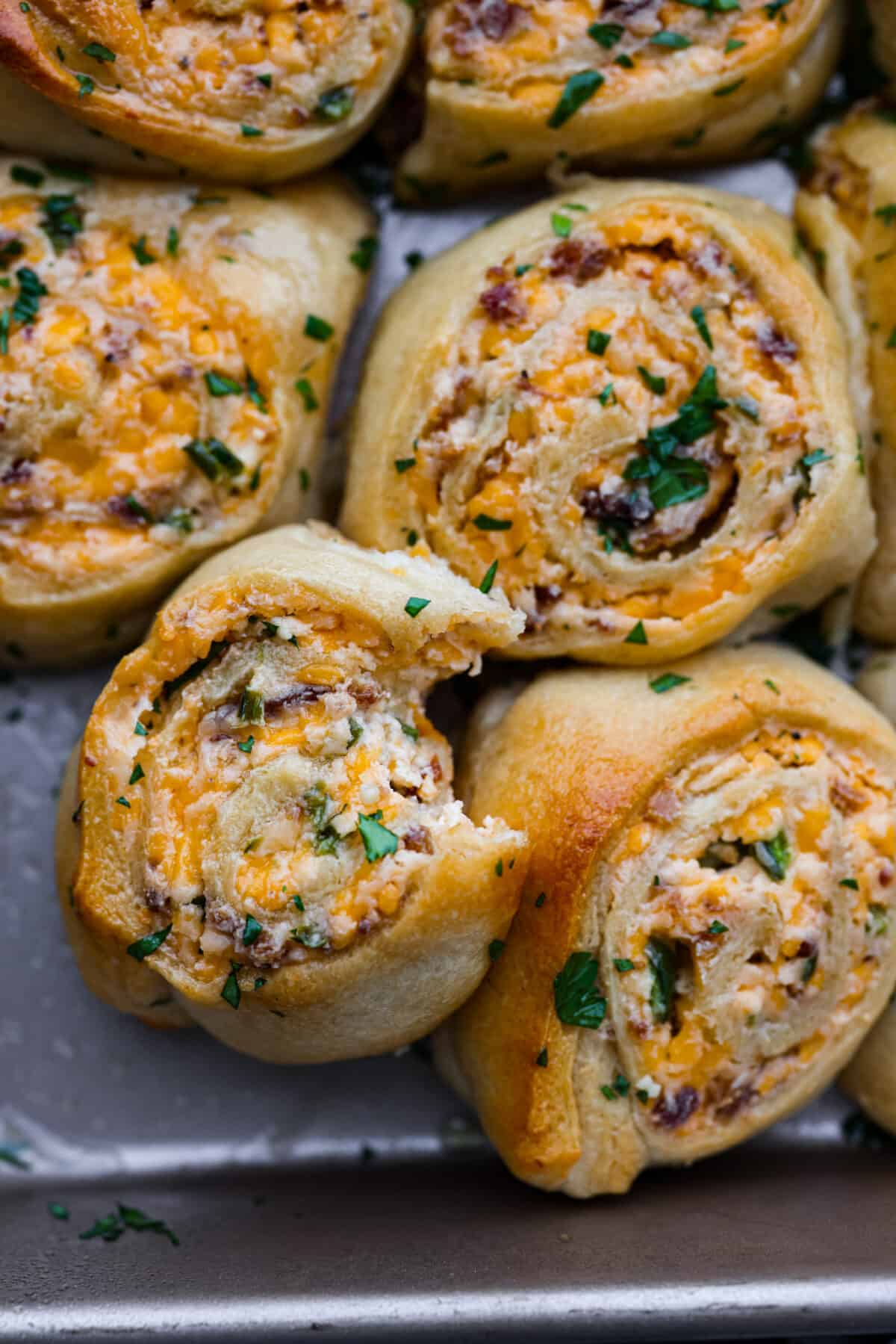 These jalapeño popper rolls are filled with a cream cheese mixture including bacon, cheese, and diced jalapeño and rolled up in crescent dough. Baked then brushed with garlic butter...everyone will devour them! Close view of a roll with a bite out of it. The roll is stacked on top of other jalapeno popper rolls.