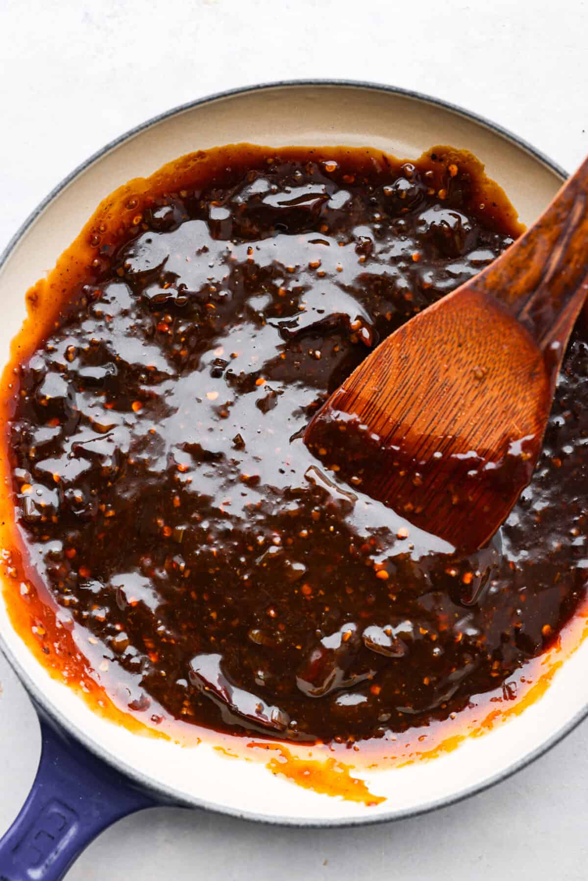 Sweet, sour, and spicy, Kung Pao Sauce is easy to make and the perfect addition for your Chinese-inspired dishes. This homemade version is so flavorful, you'll never want store-bought again! Kung pao sauce being mixed with a wooden spoon in a blue and white skillet.
