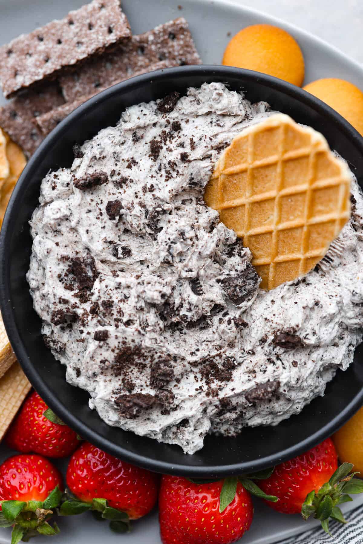 Irresistible, creamy Oreo Dip is an easy, no bake dessert dip with the most wonderful Oreo cookie flavor! Whip this treat up in just 10 minutes with Oreo cookies, cream cheese, powdered sugar, vanilla and Cool Whip. Serve with strawberries and cookies for a fun snack that's sure to be a hit! Closeup of the Oreo dip with a piece of waffle cone stuck into it.