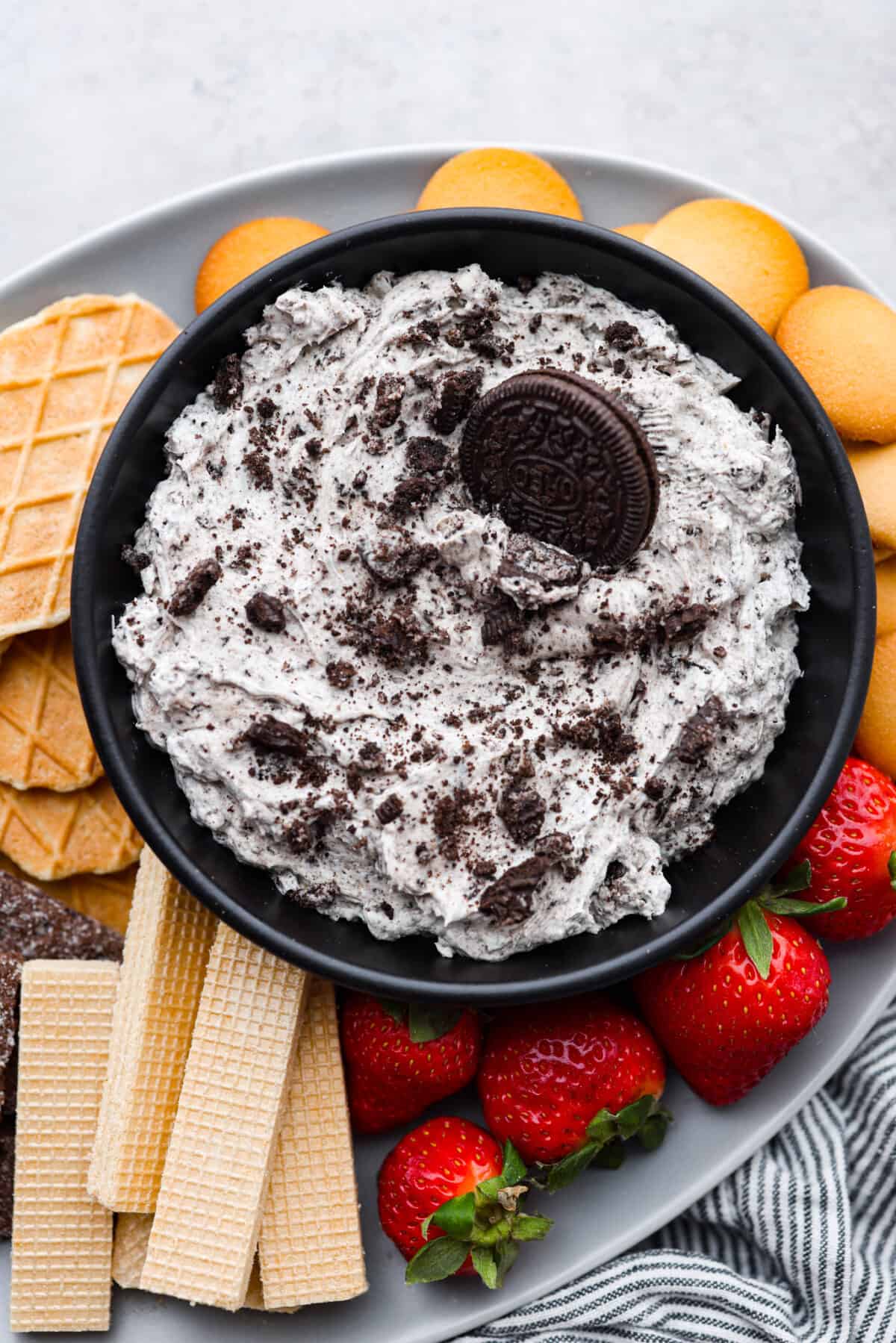 Irresistible, creamy Oreo Dip is an easy, no bake dessert dip with the most wonderful Oreo cookie flavor! Whip this treat up in just 10 minutes with Oreo cookies, cream cheese, powdered sugar, vanilla and Cool Whip. Serve with strawberries and cookies for a fun snack that's sure to be a hit! A bowl of oreo dip surrounded by cookies, wafers, and strawberries.