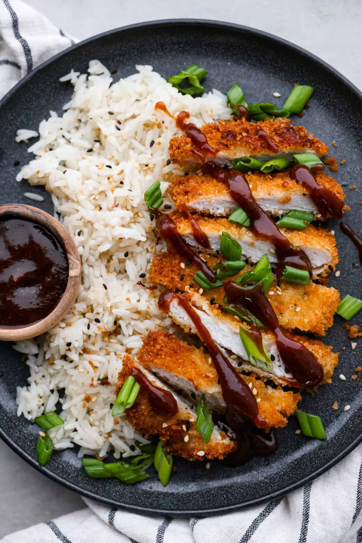 Pork loin chops flattened until thin and tender, coated in panko crumbs and fried to crispy, golden brown perfection. So delicious, this pork katsu is a comfort dish great for lunch or dinner any day of the week! Sliced pork katsu served with rice on a black plate.