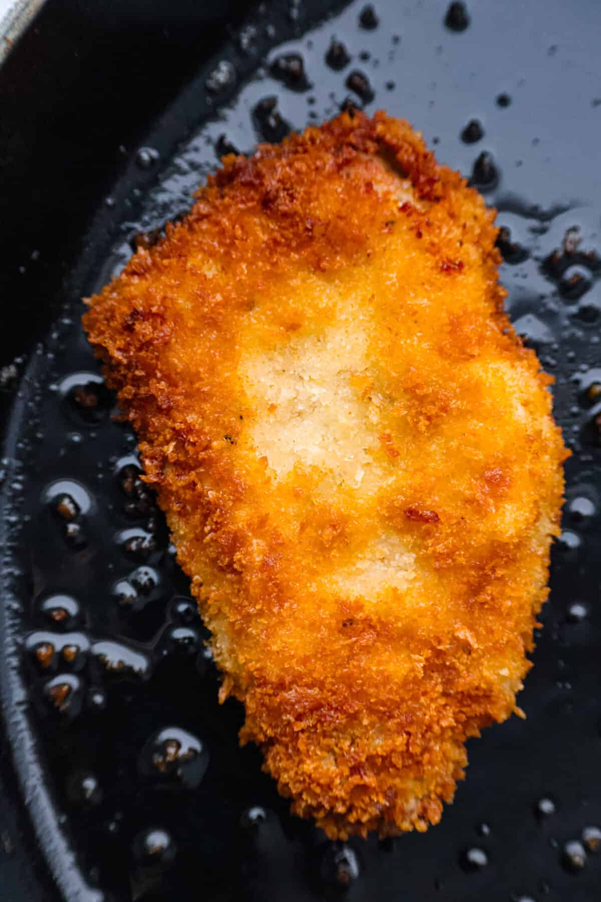 Pork loin chops flattened until thin and tender, coated in panko crumbs and fried to crispy, golden brown perfection. So delicious, this pork katsu is a comfort dish great for lunch or dinner any day of the week! Closeup of a pork cutlet being fried in oil.