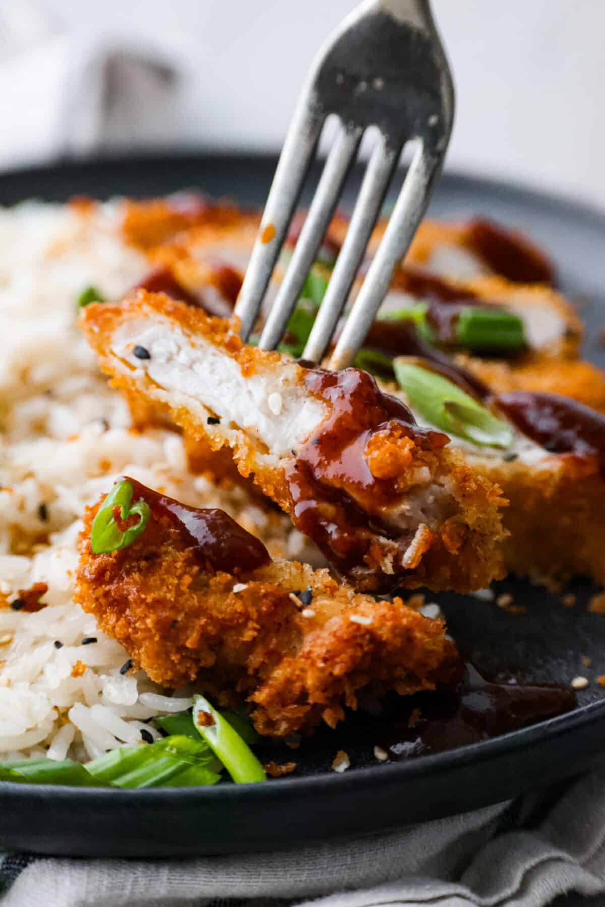 Pork loin chops flattened until thin and tender, coated in panko crumbs and fried to crispy, golden brown perfection. So delicious, this pork katsu is a comfort dish great for lunch or dinner any day of the week! Closeup of a slice of pork katsu.