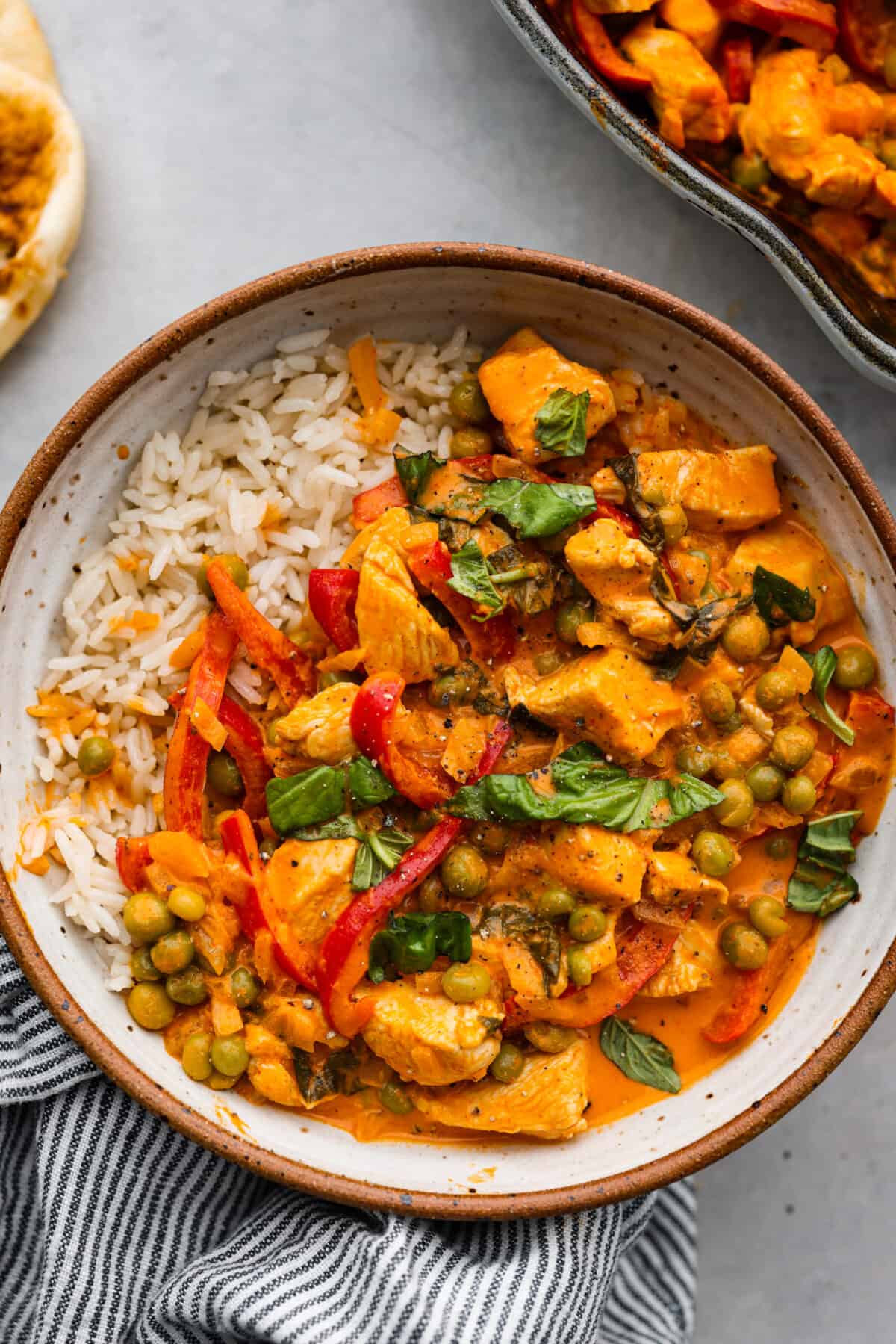 Mouthwatering Red Curry is an explosion of flavors that you're going to love! A combination of tender chicken, colorful red bell peppers, and aromatic Thai basil come together in a creamy coconut milk and curry paste sauce, for an incredibly delicious meal. A serving of red curry and white rice in a stoneware bowl.