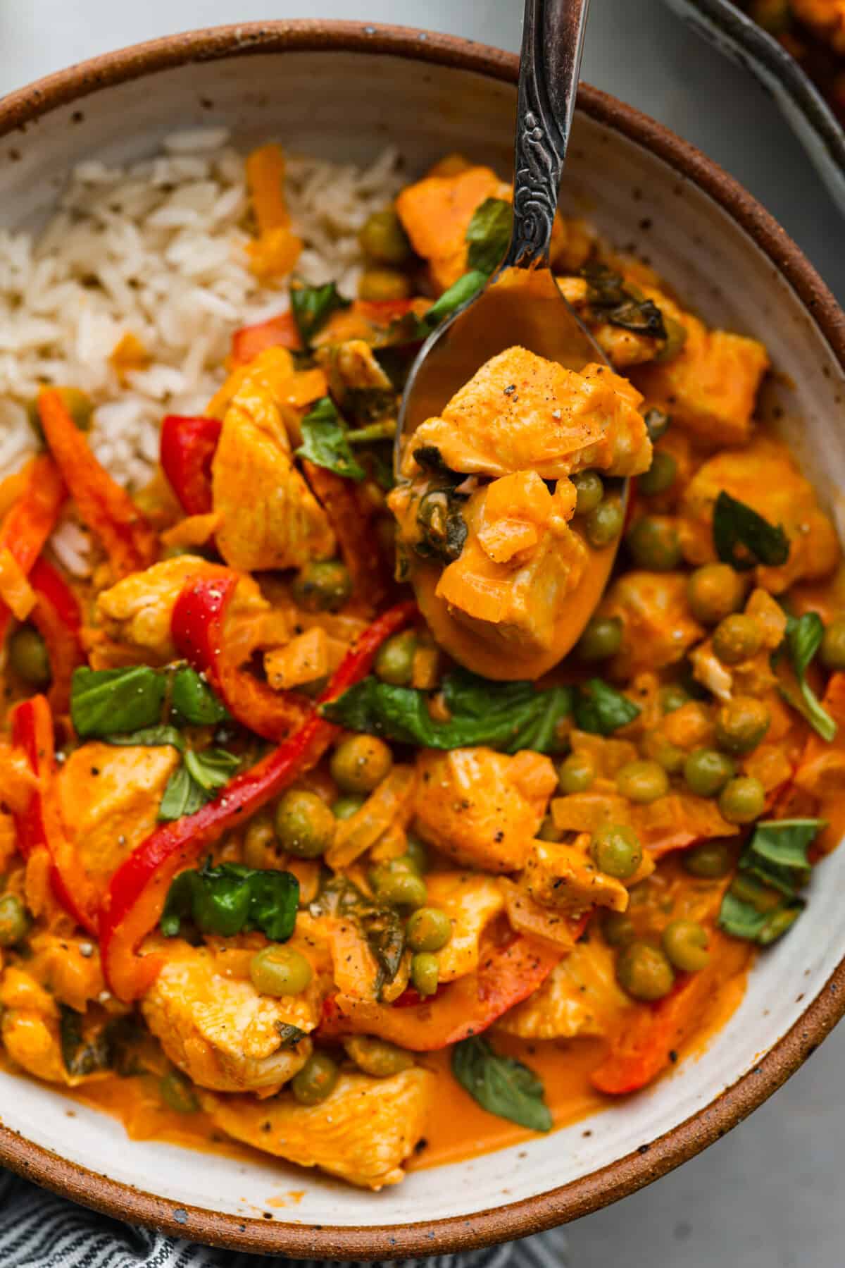 Mouthwatering Red Curry is an explosion of flavors that you're going to love! A combination of tender chicken, colorful red bell peppers, and aromatic Thai basil come together in a creamy coconut milk and curry paste sauce, for an incredibly delicious meal. Closeup of a spoonful of red curry.