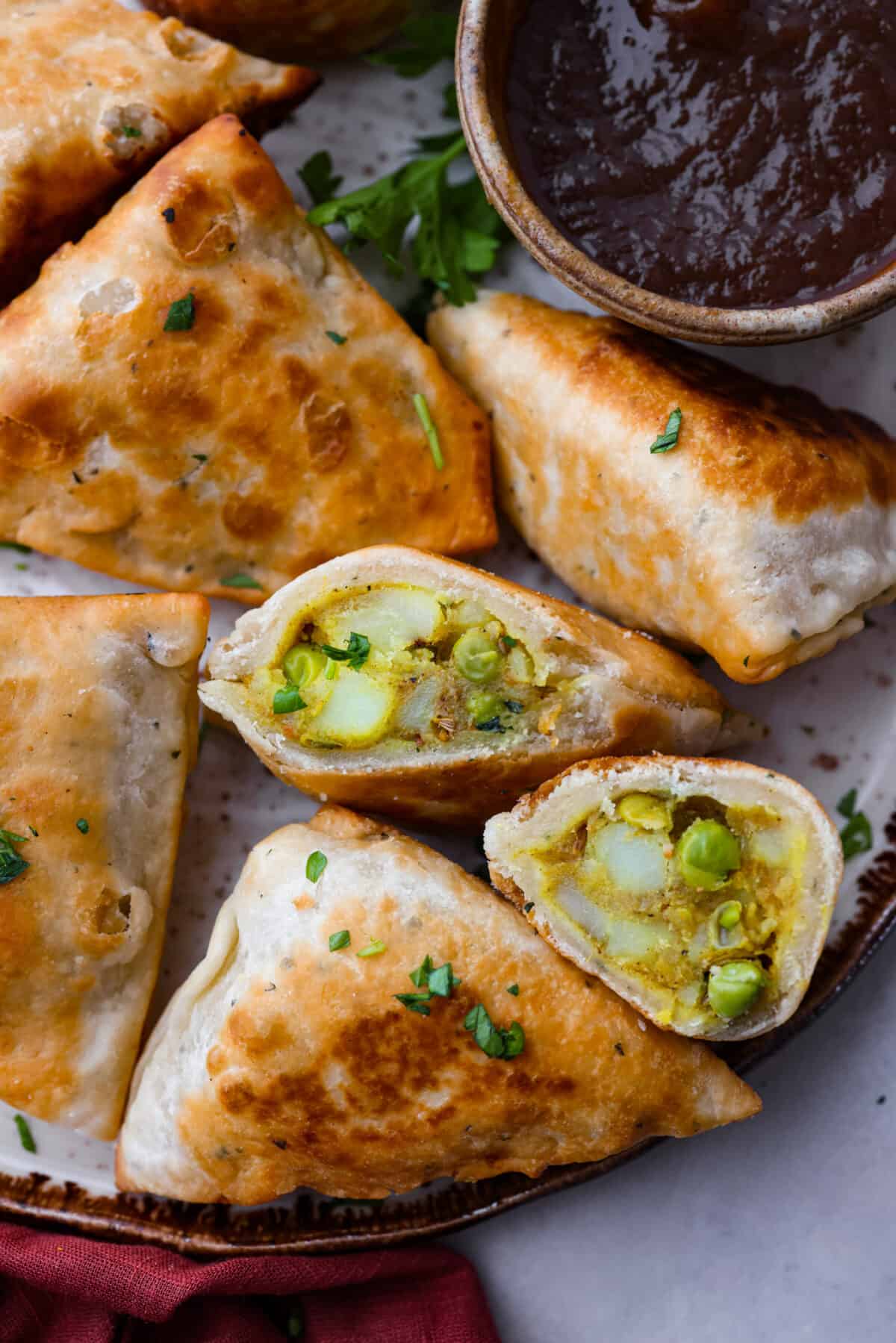 Craving some crispy, golden goodness? Look no further than these fried potato and pea samosas, seasoned to perfection with a savory curry blend. Closeup of a samosa that has been cut in half.