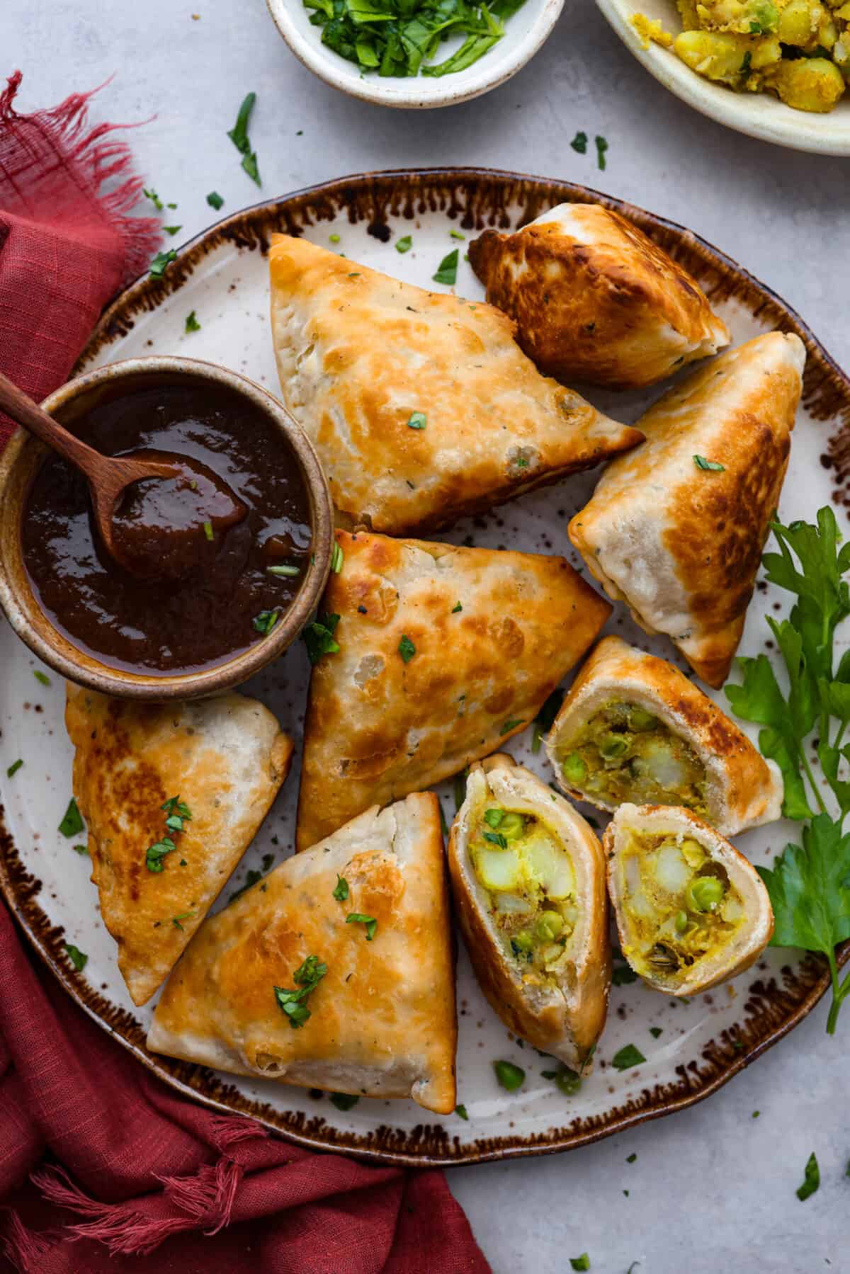 Craving some crispy, golden goodness? Look no further than these fried potato and pea samosas, seasoned to perfection with a savory curry blend. Samosas served on a plate alongside a thick red sauce.