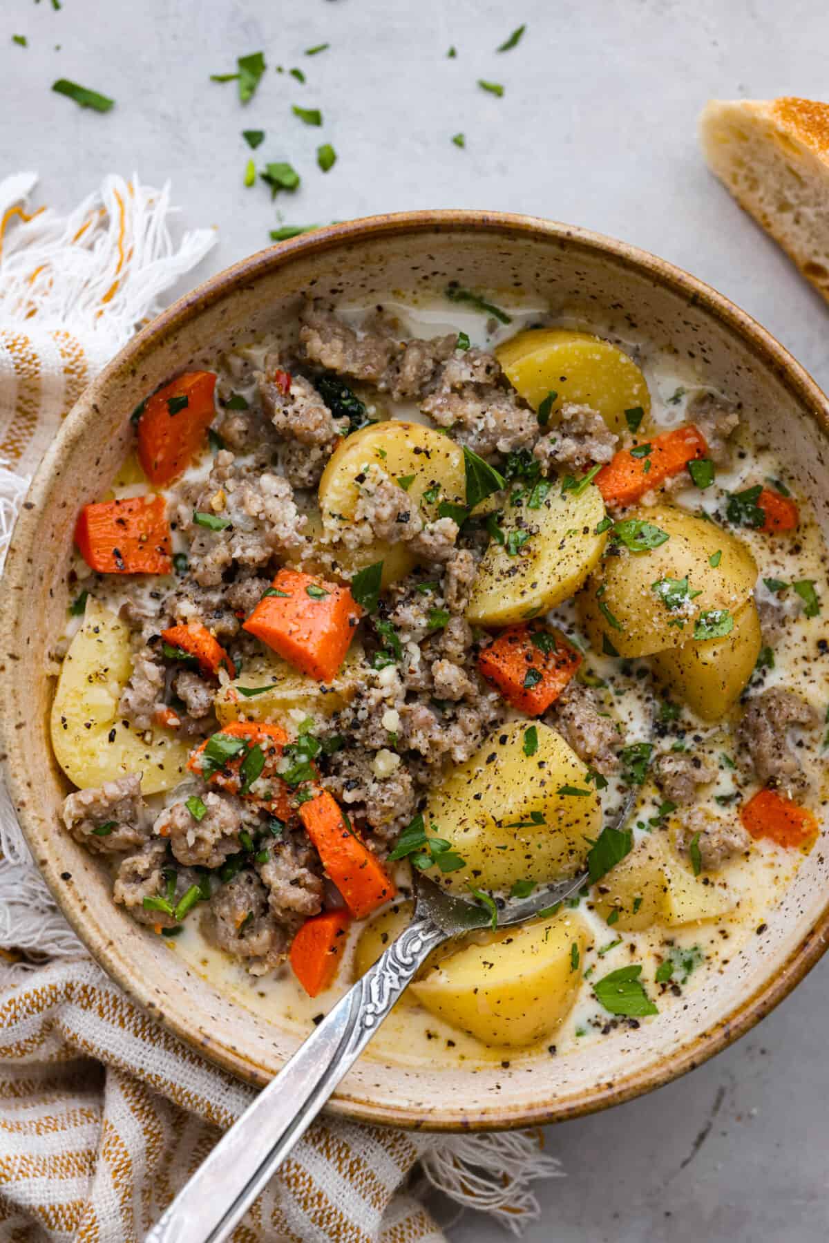 Buttery yellow potatoes and flavorful Italian sausage cooked together in a creamy, herb-filled soup base. The perfect hearty recipe to warm you up from the inside-out! A serving of sausage and potato soup in a stoneware bowl.