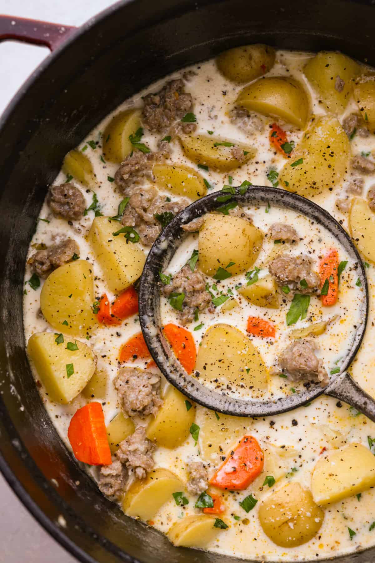 Buttery yellow potatoes and flavorful Italian sausage cooked together in a creamy, herb-filled soup base. The perfect hearty recipe to warm you up from the inside-out! Creamy sausage and potato soup in a large pot, being scooped up with a ladle.