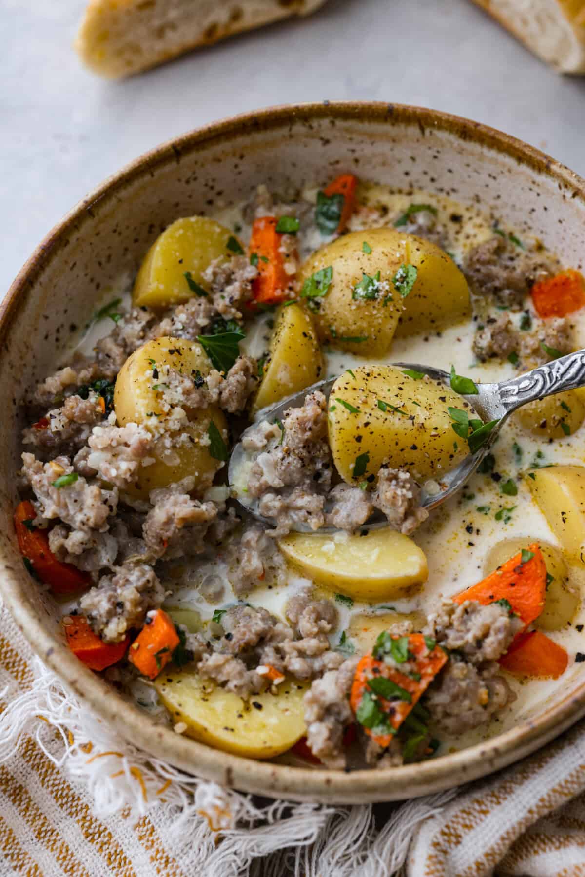 Buttery yellow potatoes and flavorful Italian sausage cooked together in a creamy, herb-filled soup base. The perfect hearty recipe to warm you up from the inside-out! Closeup of a serving of soup.