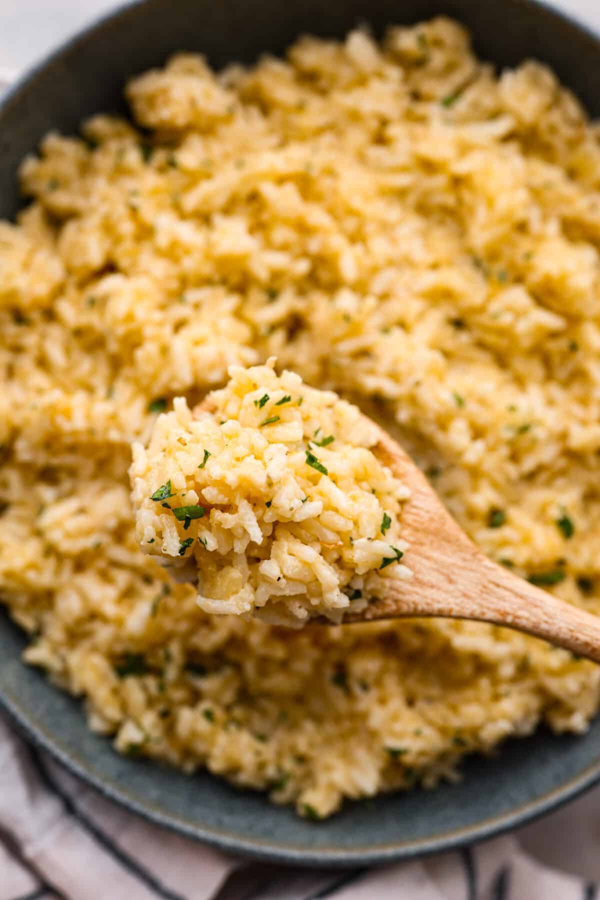 Make mealtime a breeze with this easy Souper Rice recipe! Combine creamy chicken soup, instant white rice, Parmesan cheese, and Italian seasonings for a quick and tasty dish. Simple, delicious, and a side dish that is ready in no time! A close up of super rice scooped onto a wooden spoon.