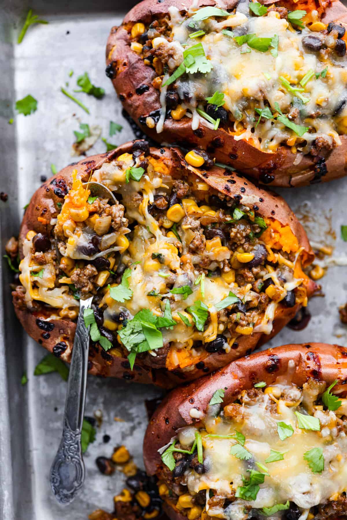 All your favorite taco fixings stuffed inside soft, tender sweet potatoes. This is a hearty, delicious dinner the whole family will love! It's meaty, cheesy, and extremely satisfying. Top-down view of 3 stuffed sweet potatoes.