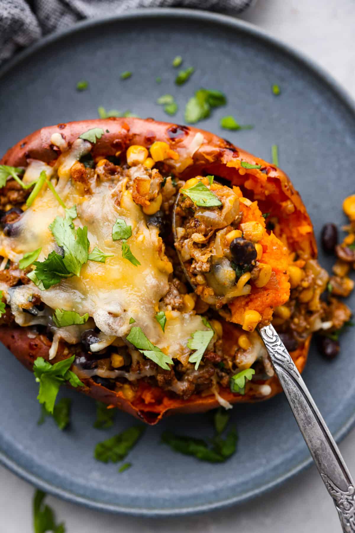 All your favorite taco fixings stuffed inside soft, tender sweet potatoes. This is a hearty, delicious dinner the whole family will love! It's meaty, cheesy, and extremely satisfying. Taking a spoonful of roasted sweet potato and the filling.