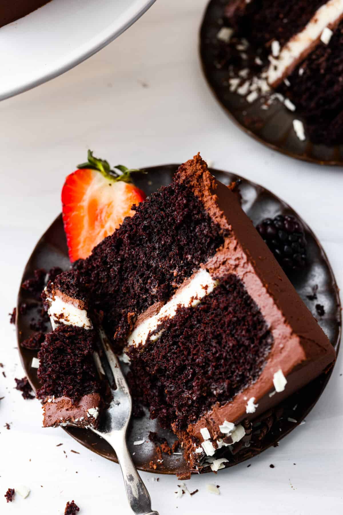 Chocolate lovers, this tuxedo cake is for you! Two layers of moist chocolate cake wrapped in chocolate and white chocolate ganache. So rich and delicious, it's almost sinful. A slice of chocolate cake on a black plate with a bite taken out of it.