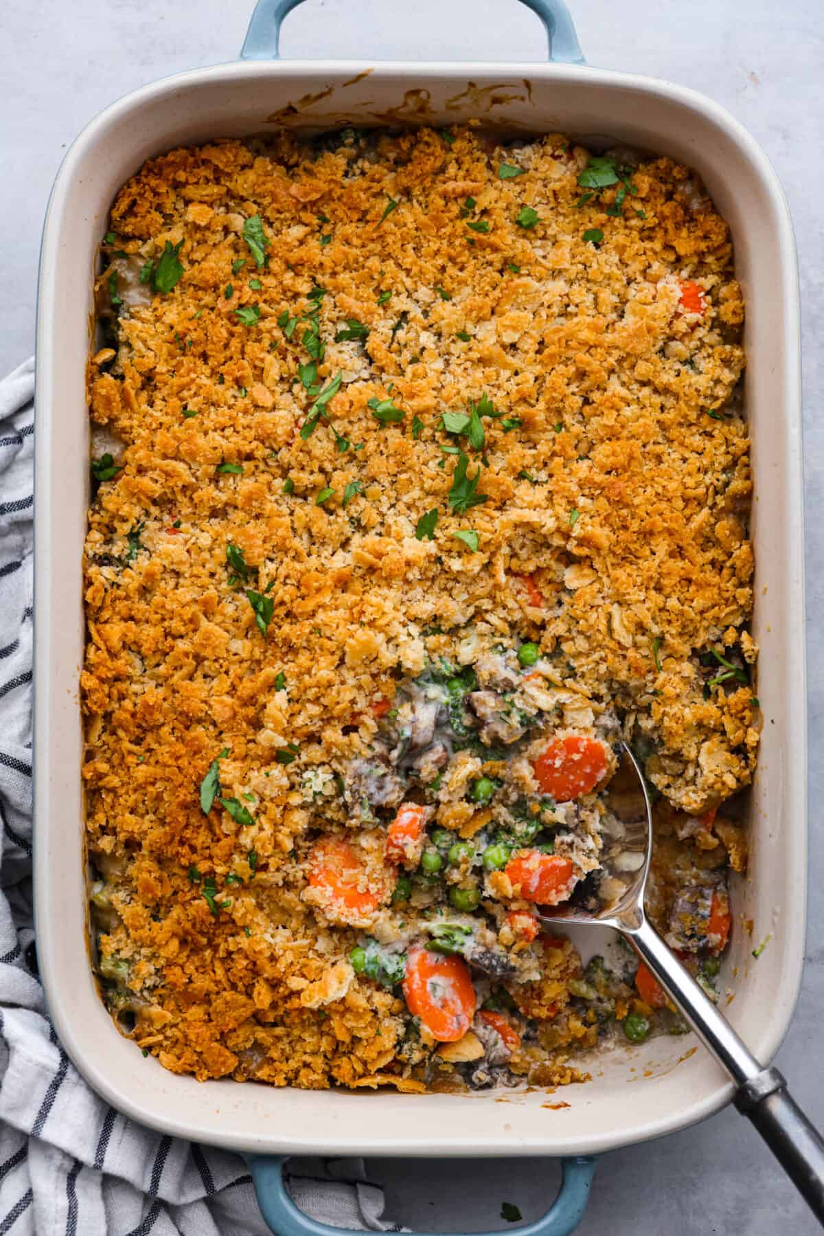 Delicious Vegetable Casserole is wonderfully creamy, flavorful and loaded up with tender broccoli florets, carrots, mushrooms and peas. It's topped with crispy buttered Ritz cracker crumbs, and baked to golden brown perfection. A dish that's sure to be the highlight of your dinner! Serving a scoop of vegetable casserole.