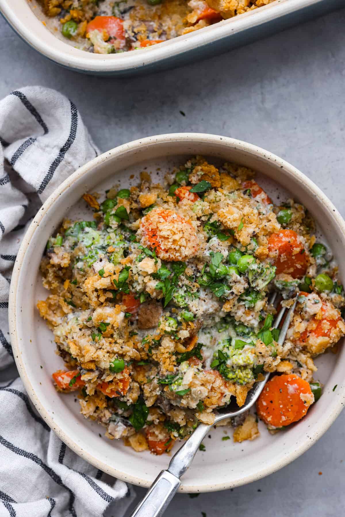 Delicious Vegetable Casserole is wonderfully creamy, flavorful and loaded up with tender broccoli florets, carrots, mushrooms and peas. It's topped with crispy buttered Ritz cracker crumbs, and baked to golden brown perfection. A dish that's sure to be the highlight of your dinner! A serving of casserole in a white bowl.