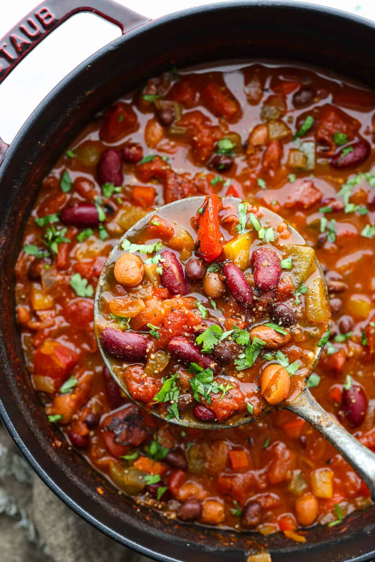 Introducing the ULTIMATE vegetarian chili recipe! It's full of tender vegetables, a combination of beans, and loaded with seasonings. It's an easy one-pot chili bursting with so many flavors and textures that you won't even miss the meat! Close overhead view of vegetarian chili in a large pot. A ladle is lifting up a scoop of chili.