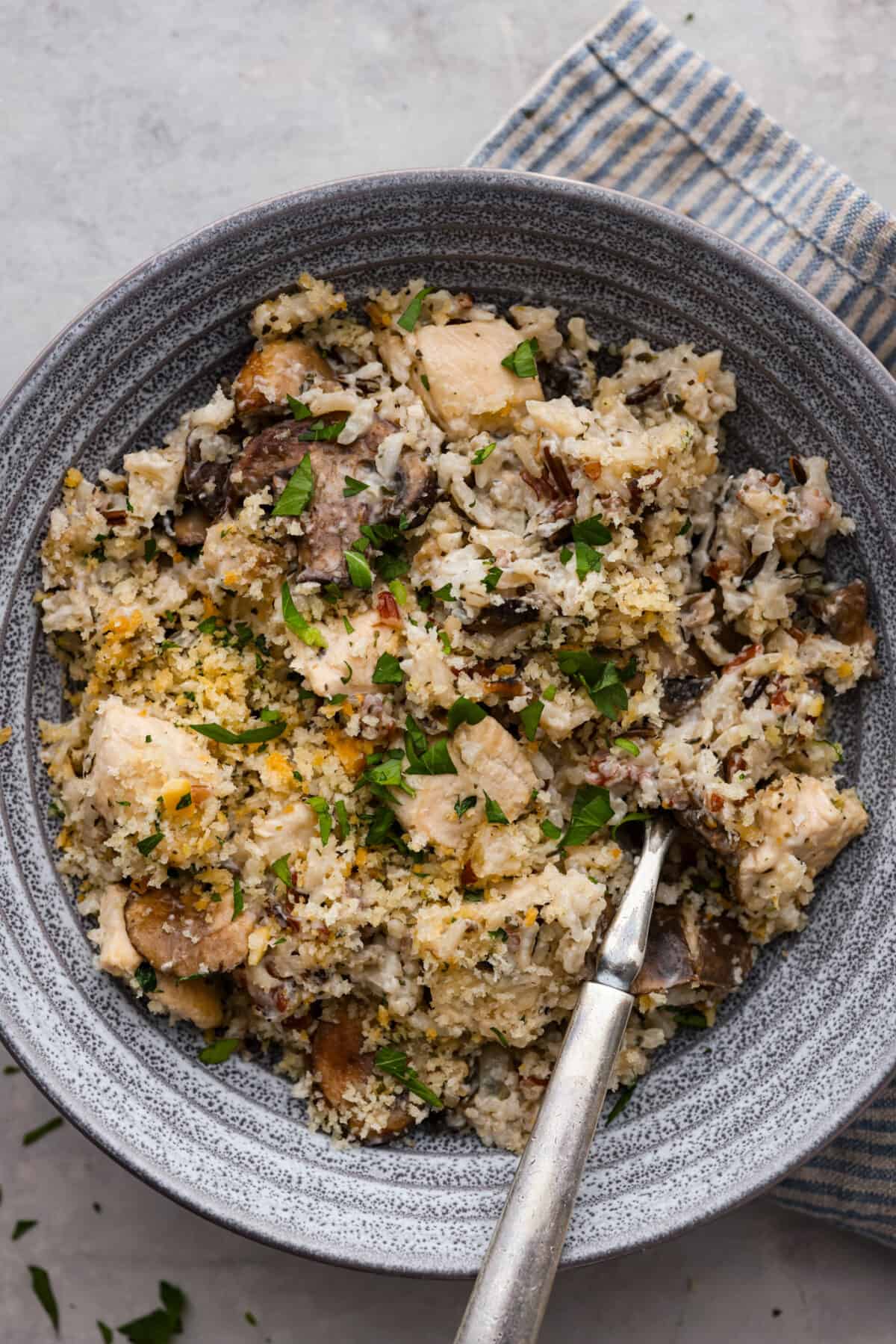Chicken and wild rice casserole is an easy, comforting meal that the whole family will enjoy! You just can't go wrong with tender chicken and wild rice in a creamy sauce, and topped off with buttery breadcrumbs. A serving of the casserole in a gray stoneware dish.