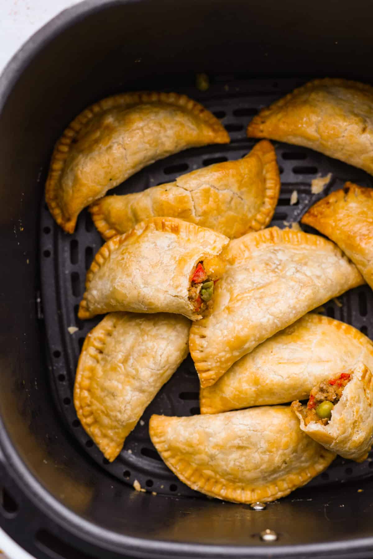 Empanadas made easy by cooking them in the air fryer and using premade pie crusts for the dough! Empanadas in the basket of an air fryer.