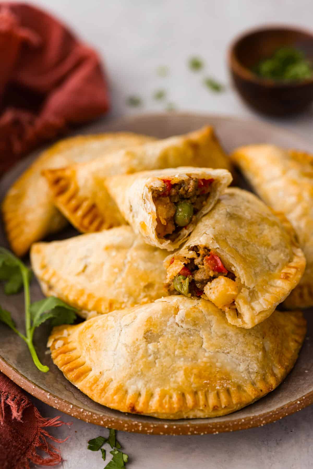 Empanadas made easy by cooking them in the air fryer and using premade pie crusts for the dough! Air fryer empanadas on a serving dish. One is broken in half so you can see the filling.