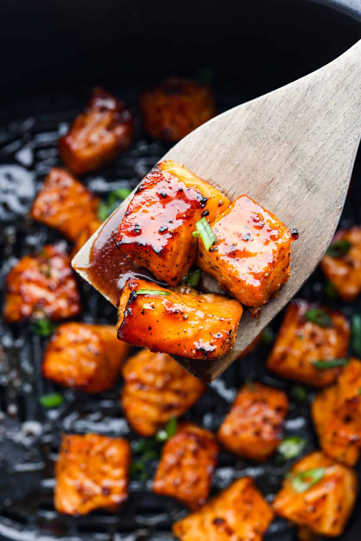 Cooked in less than 10 minutes, these perfectly glazed honey garlic air fryer salmon bites are so delicious. This is such a quick dinner, you will never want to cook salmon any other way! Close view of a wood spatula lifting up salmon bites in the air fryer.