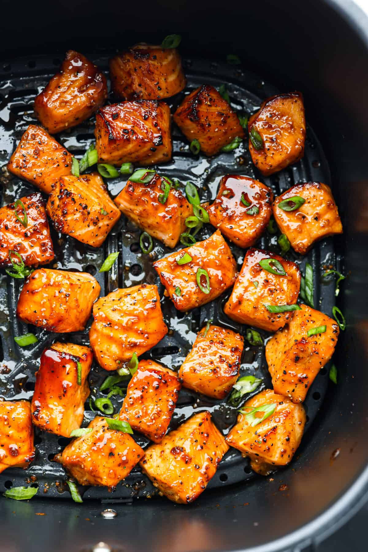 Cooked in less than 10 minutes, these perfectly glazed honey garlic air fryer salmon bites are so delicious. This is such a quick dinner, you will never want to cook salmon any other way! Top view of cooked salmon bites in the air fryer garnished with green onions.