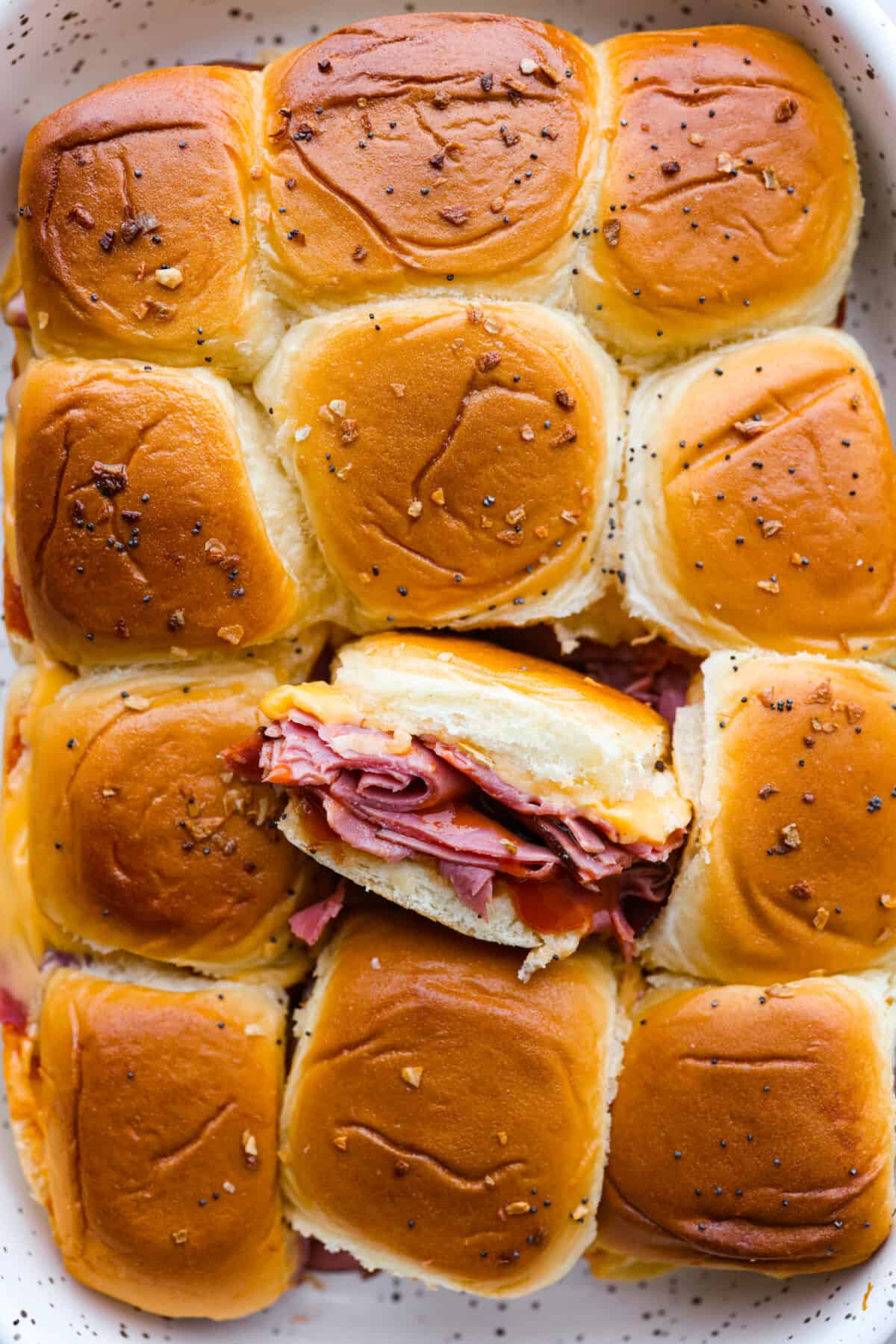 These copycat Arby's beef and cheddar sliders are a must-make for your next gathering. Soft Hawaiian buns topped with sliced roast beef, melty American cheese, onion flakes, and homemade Arby's sauce, brushed with a buttery glaze. Top-down view of Arbyโs copycat beef and cheddar sliders in a baking dish.
